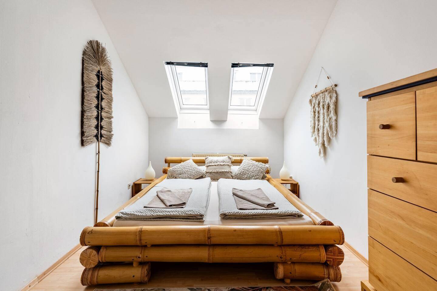 Helles Schlafzimmer im Dachgeschoss mit Bambusbett, Holzkommode und zwei Dachfenstern.