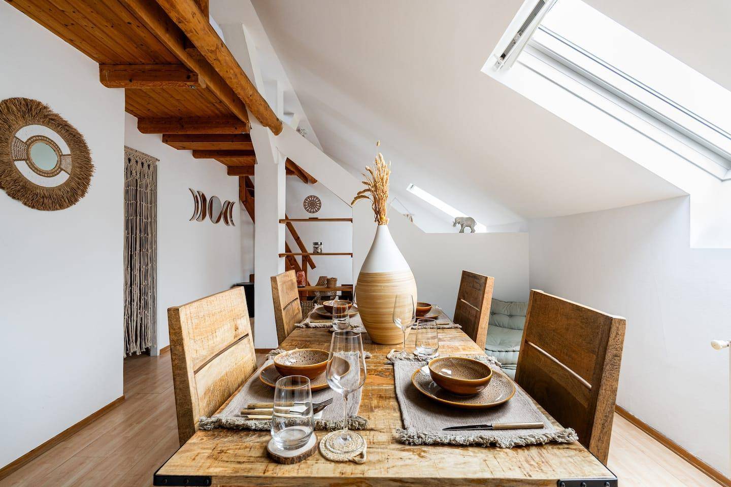 Rustikaler Essbereich im Dachgeschoss mit großem Holztisch, Holzbalken und Dachfenster.