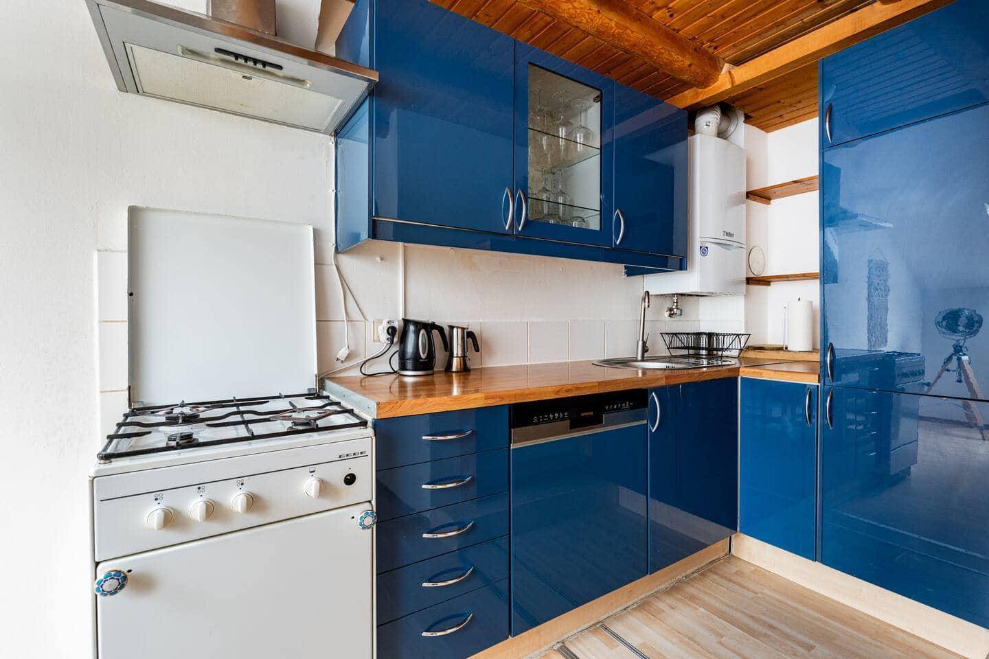 Moderne Küche mit glänzenden blauen Schränken, Holztheke und Gasherd unter Holzbalken.