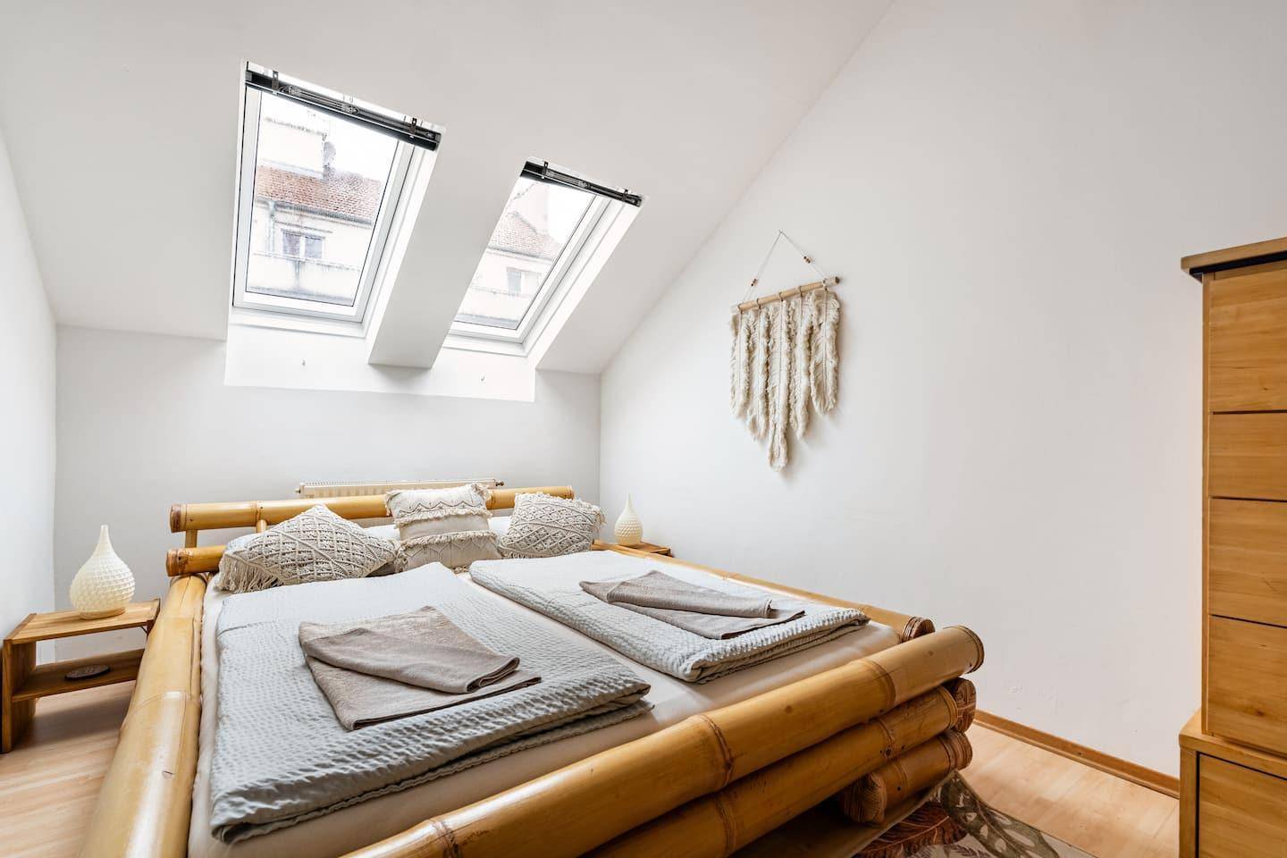 Helles Schlafzimmer im Dachgeschoss mit Bambusbett, Holzkommode und zwei Dachfenstern.