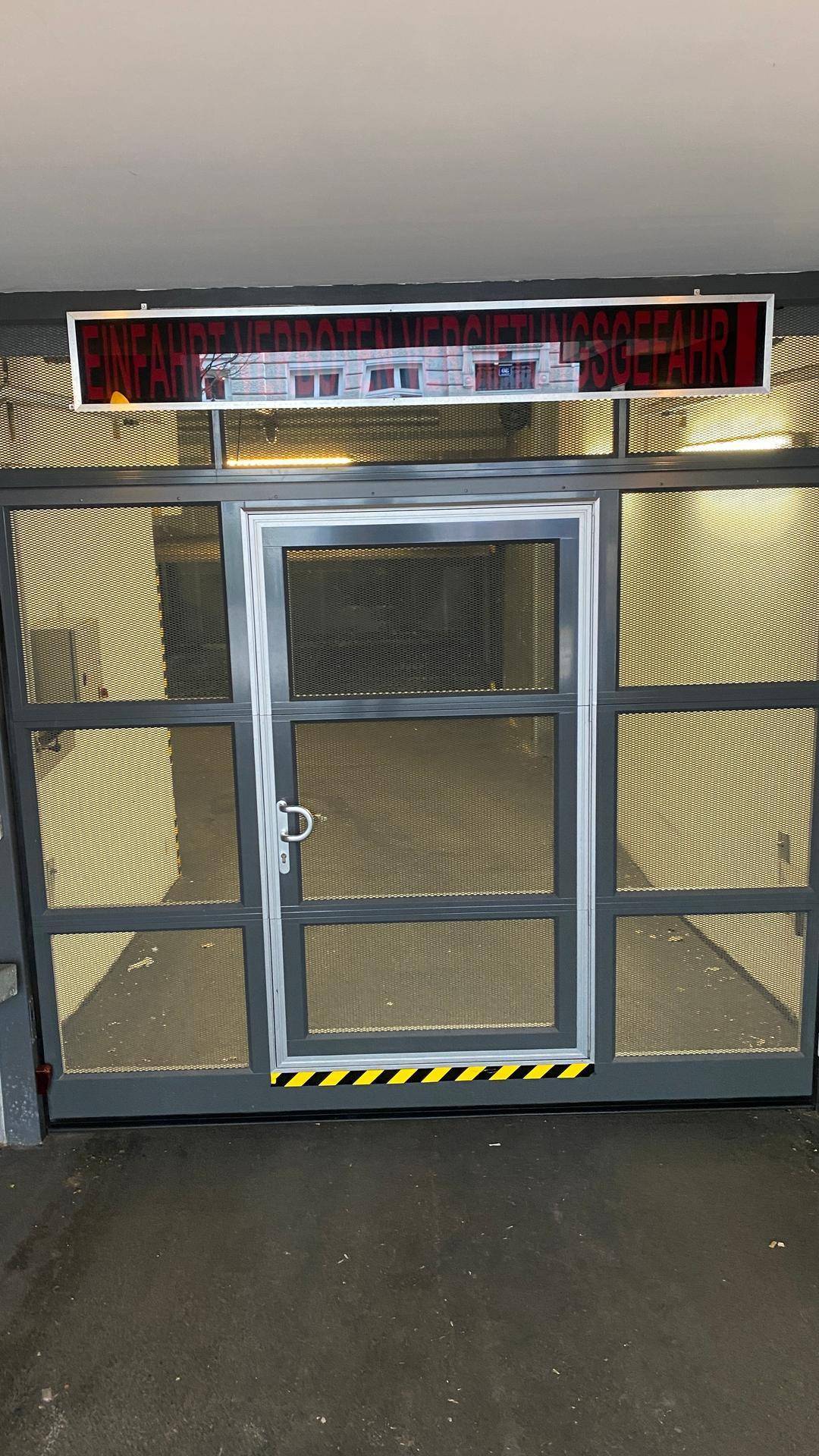 Automatisches Garagentor mit Warnhinweis und gelb-schwarzer Markierung für die Einfahrt.