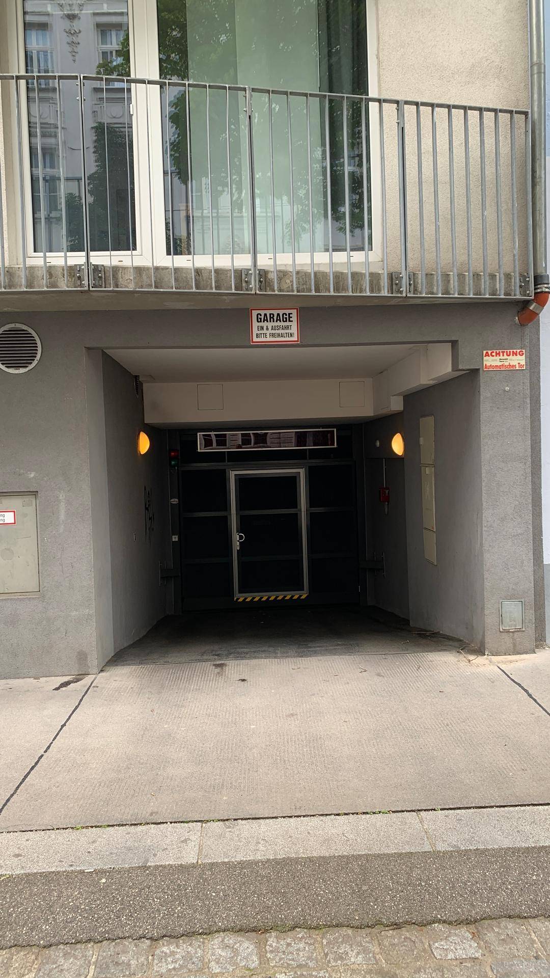 Eingang zu einer Tiefgarage mit Rampe unter einem Balkon an der Gebäudefassade.