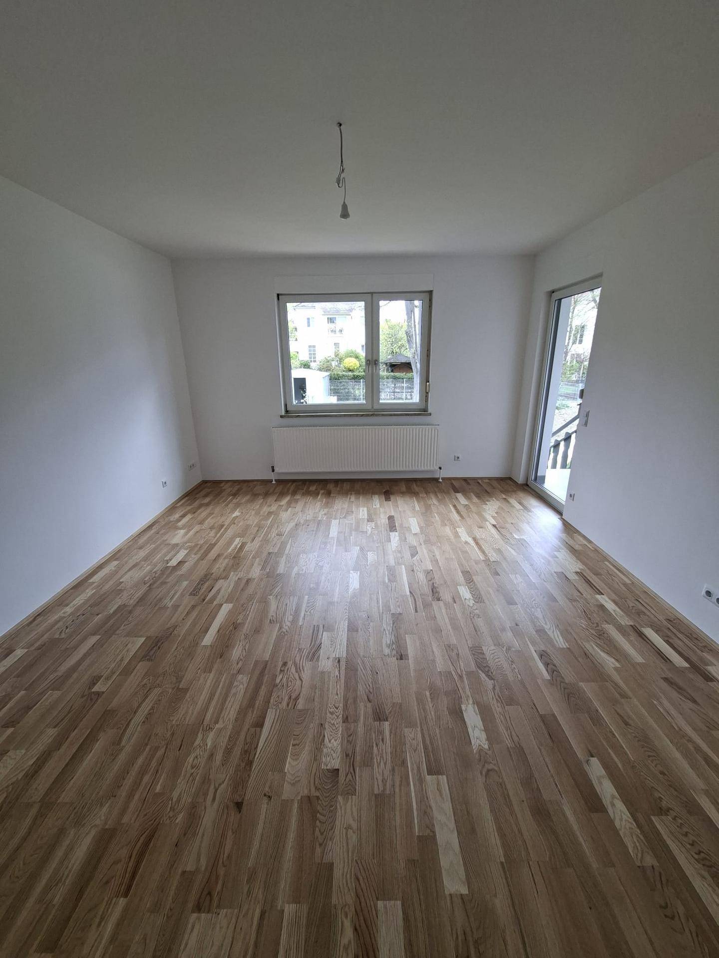 Helles Wohnzimmer mit Parkettboden, Fenster und Zugang zum Außenbereich.