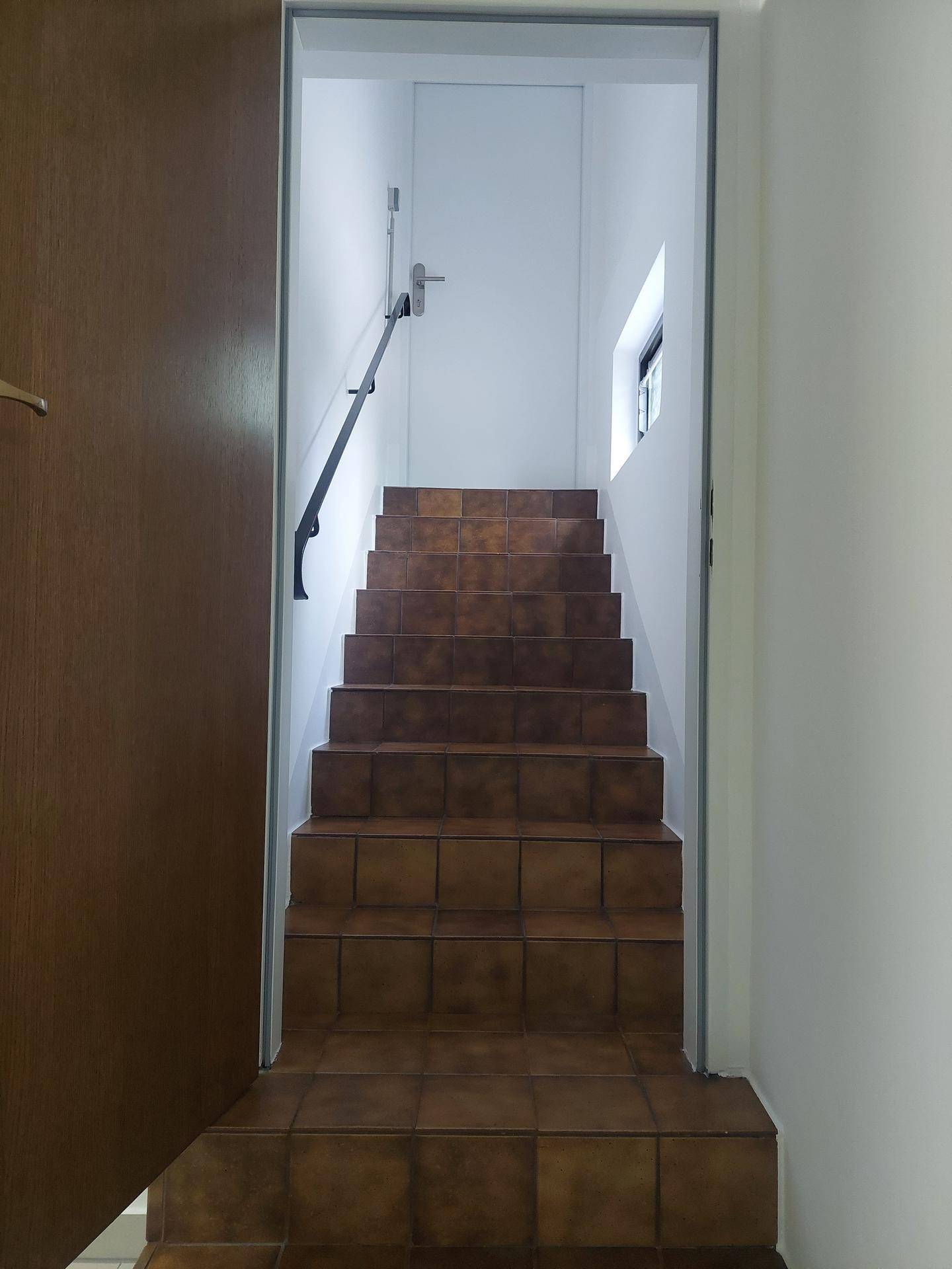 Geflieste Treppe mit dunklem Geländer führt in ein oberes Stockwerk.