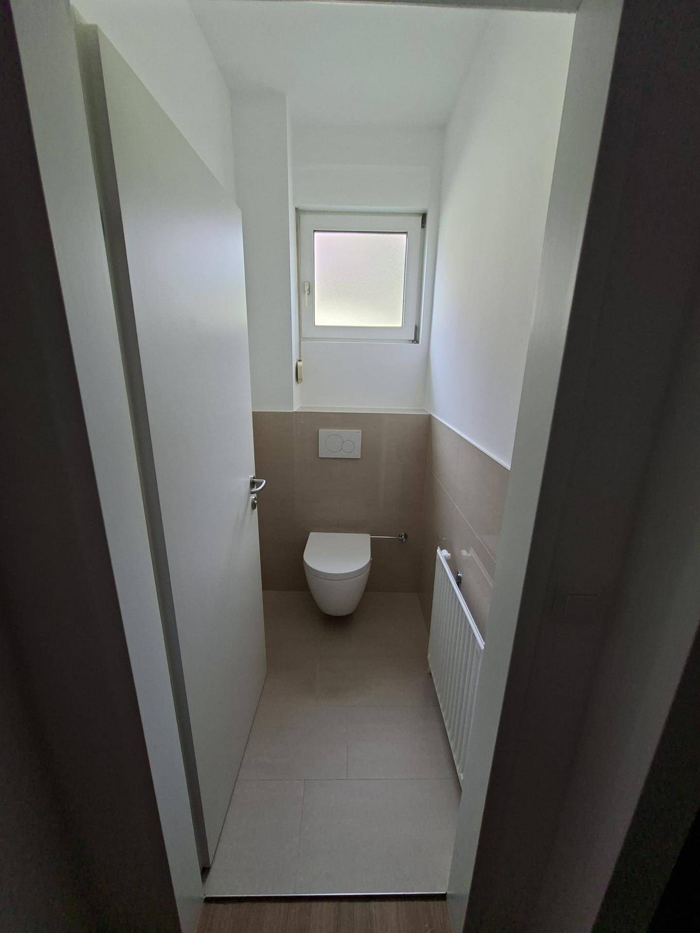 Separates Gäste-WC mit wandhängender Toilette und kleinem Fenster.