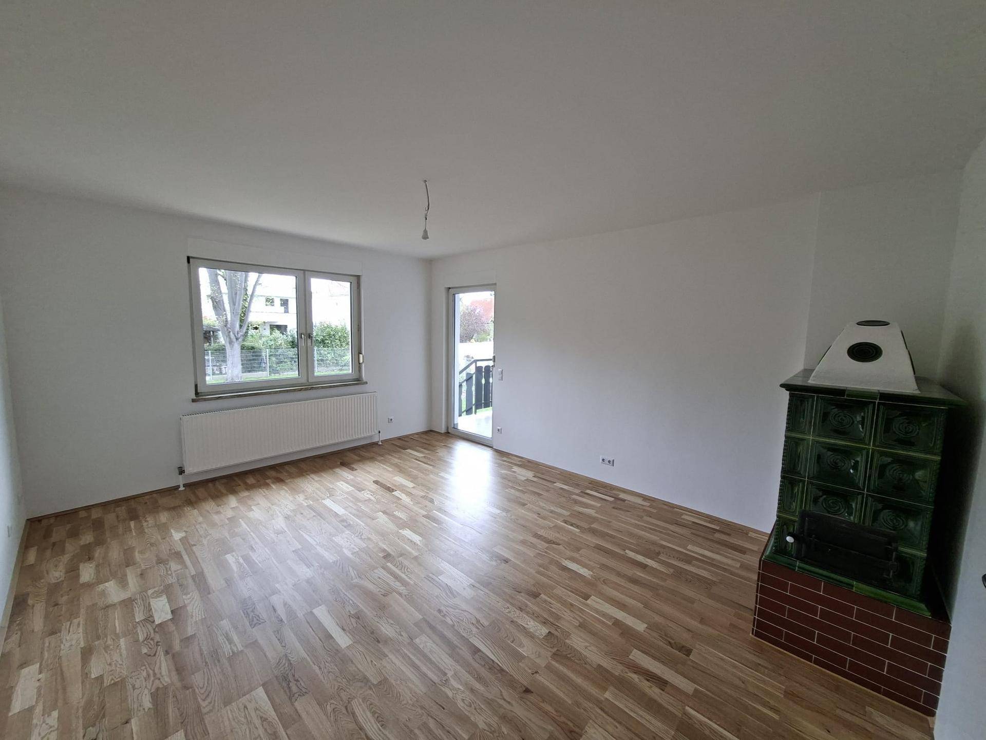 Wohnzimmer mit Kachelofen, Parkettboden und Zugang zu einem Außenbereich.