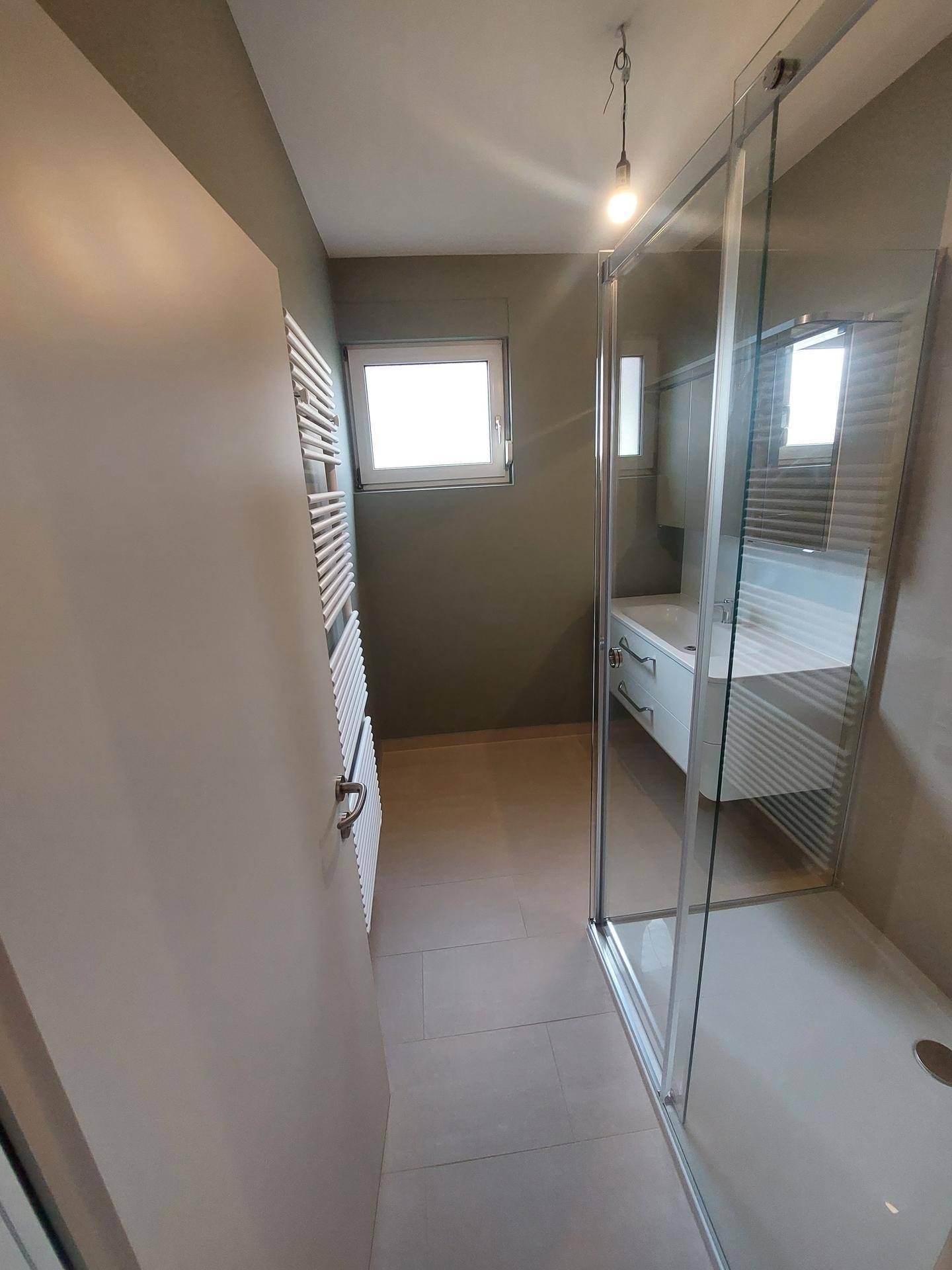 Modernes Badezimmer mit Duschkabine, Waschbecken und beheiztem Handtuchhalter.