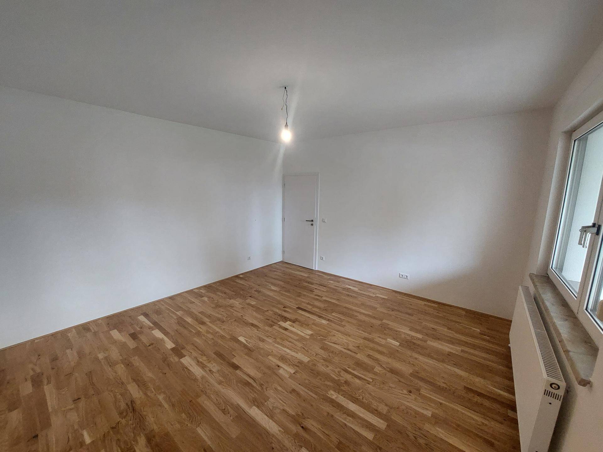 Helles Schlafzimmer mit Parkettboden und einem großen Fenster, bereit zur Einrichtung.
