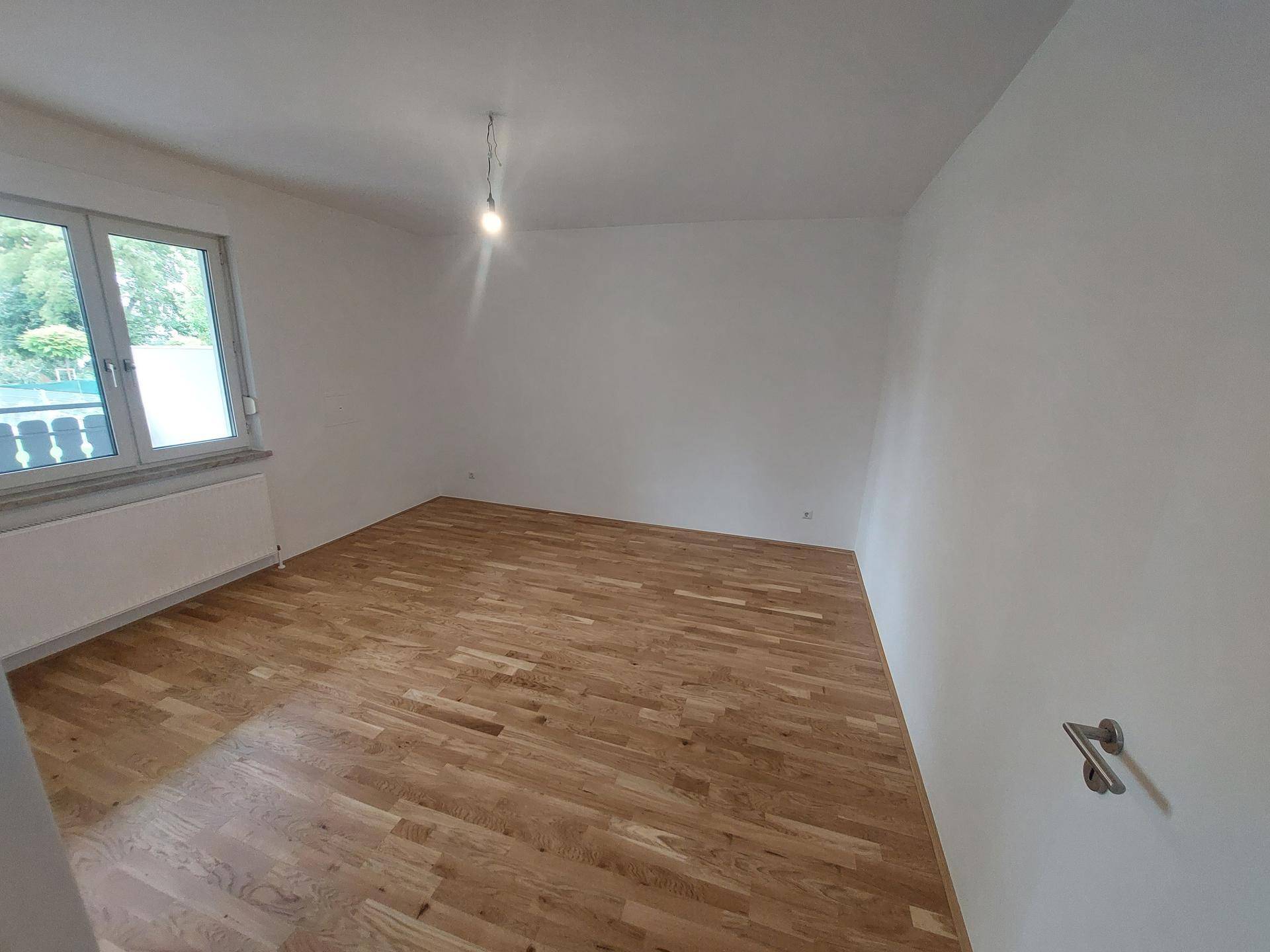 Geräumiges Schlafzimmer mit Parkettboden und Blick ins Grüne durch das Fenster.