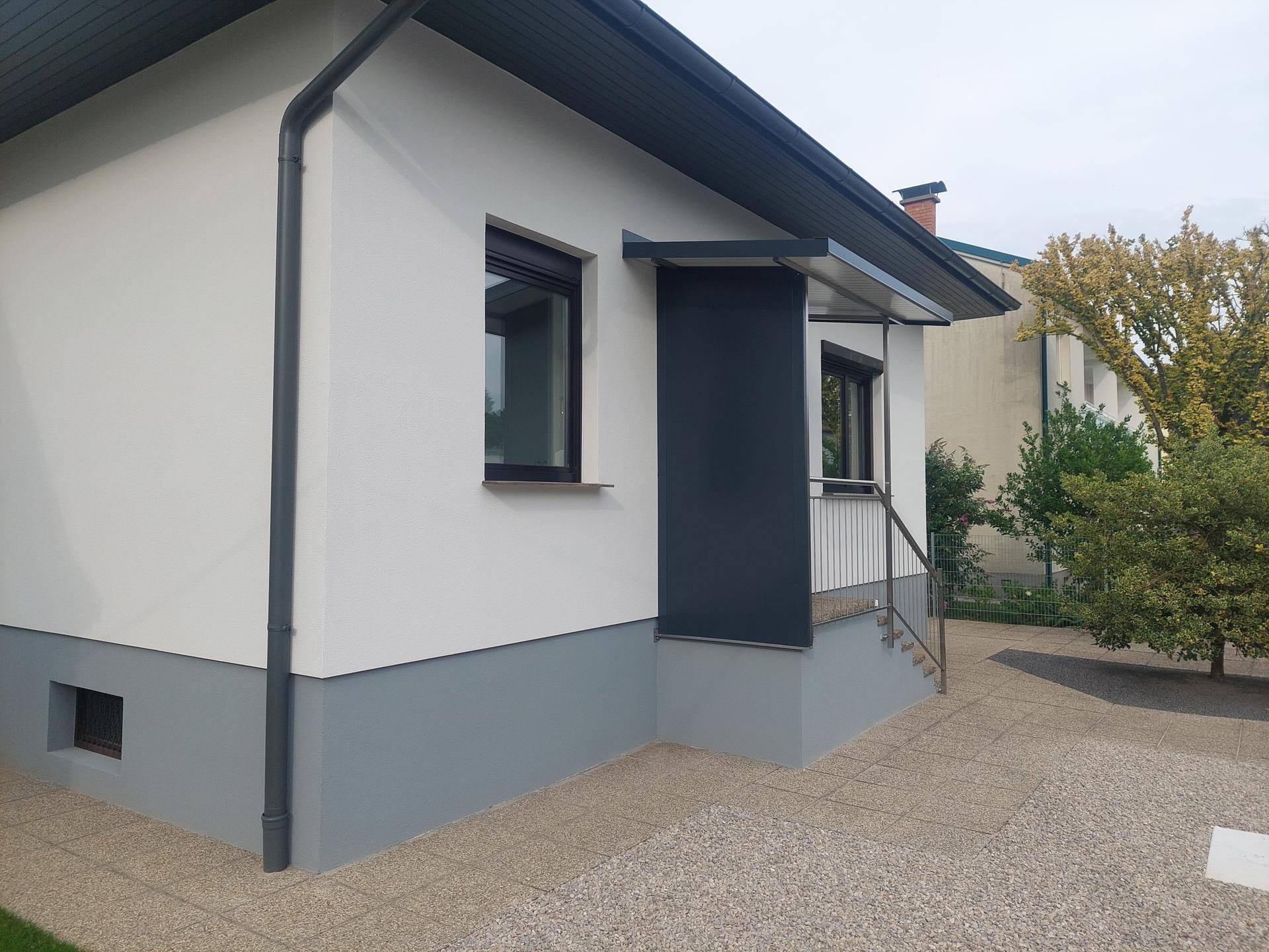 Seitenansicht des Hauses mit schlichter Fassade und Regenrinne.