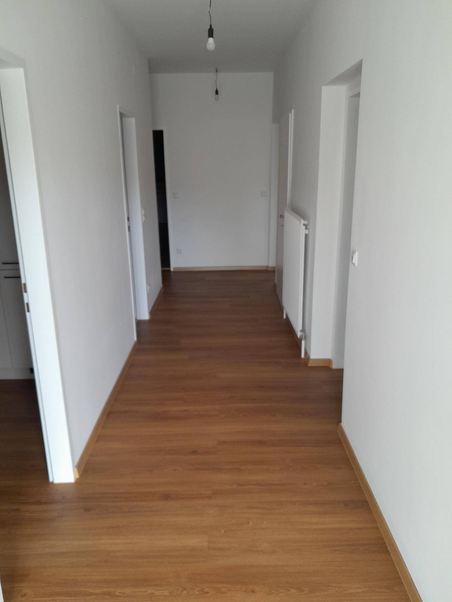 Heller Flur mit Laminatboden und weißen Wänden, der zu weiteren Räumen führt.
