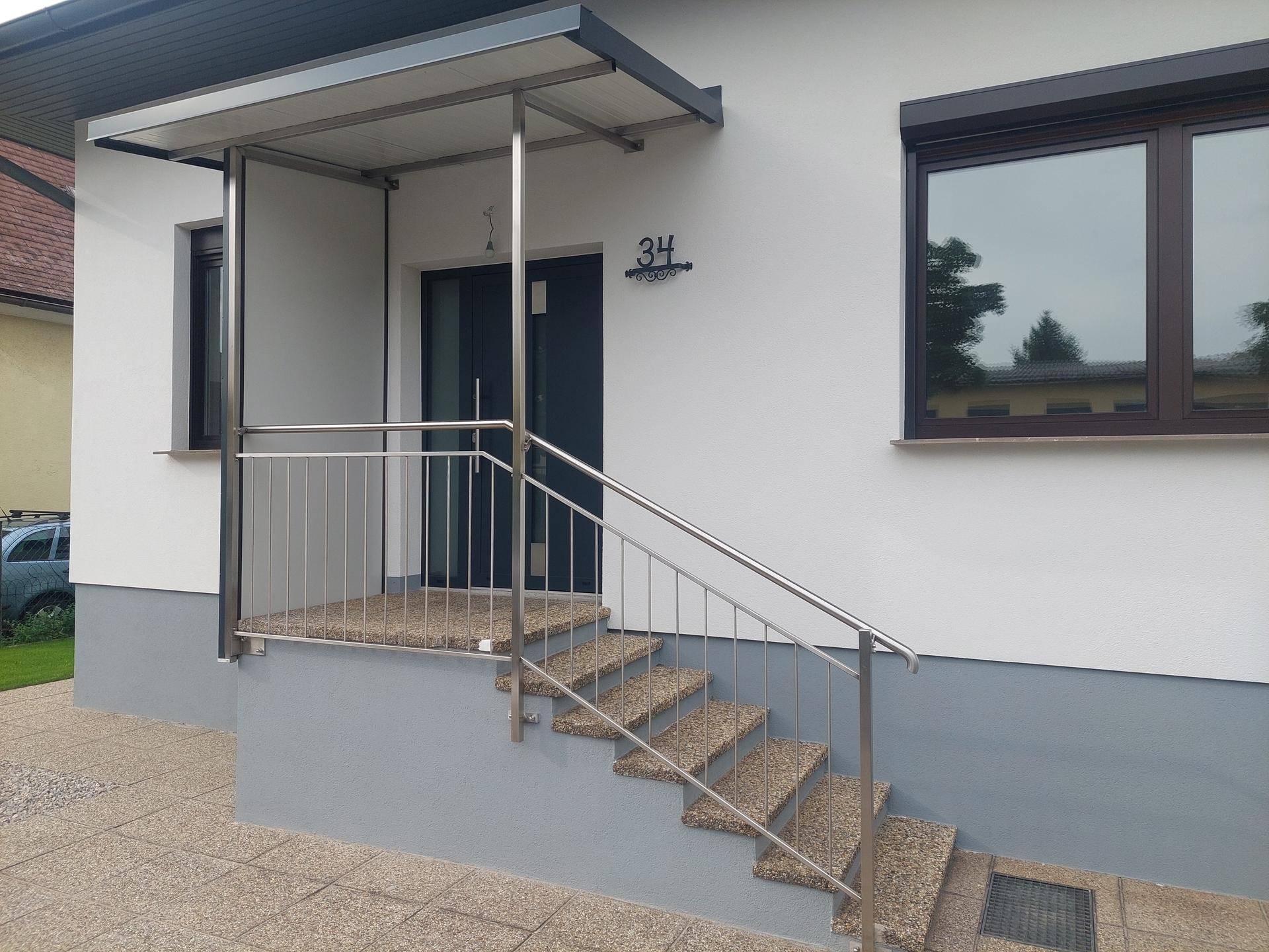 Detailansicht des Hauseingangs mit Treppe, Geländer und Vordach.