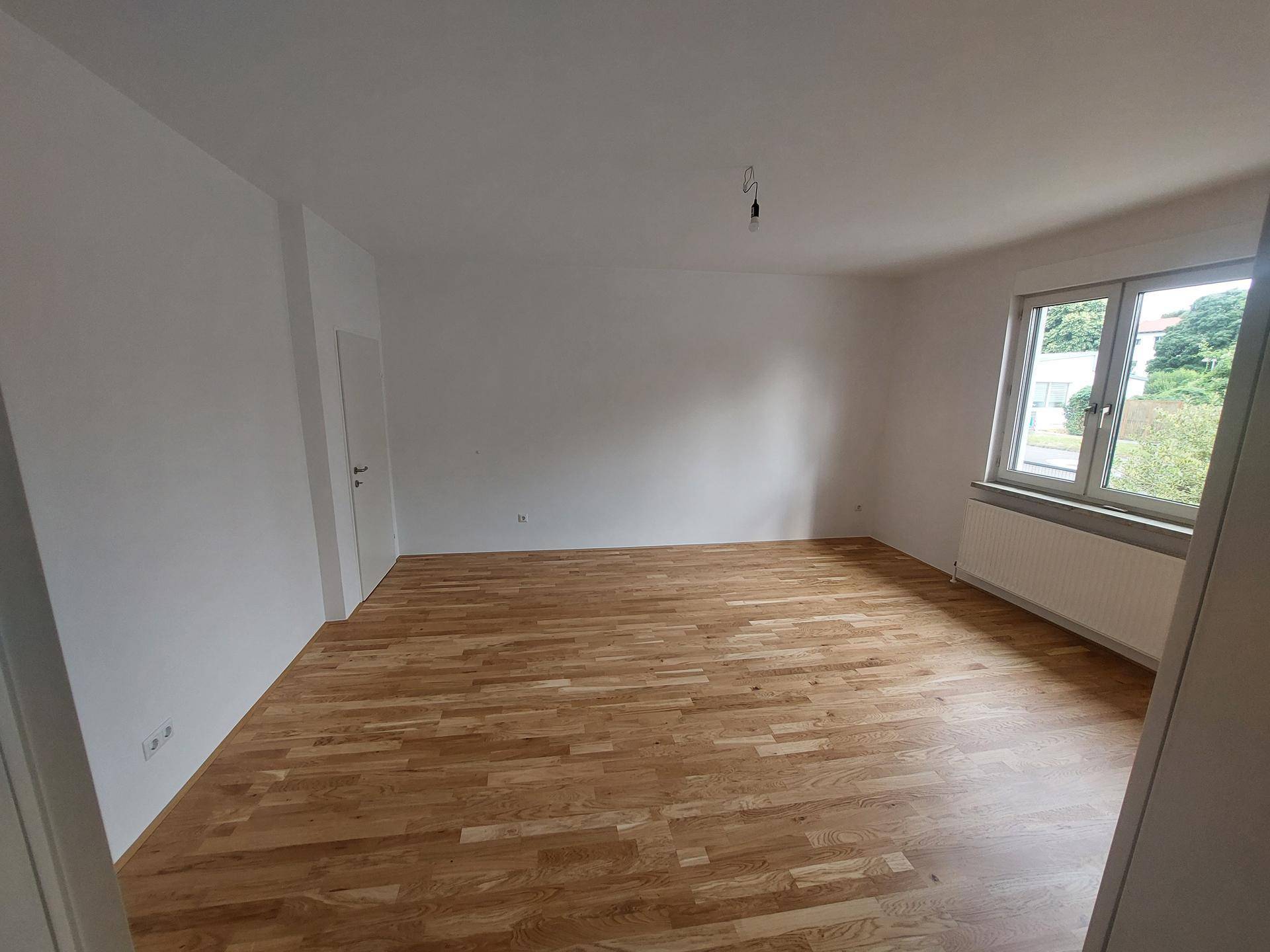 Geräumiges Wohnzimmer mit hellem Parkettboden und großen Fenstern.