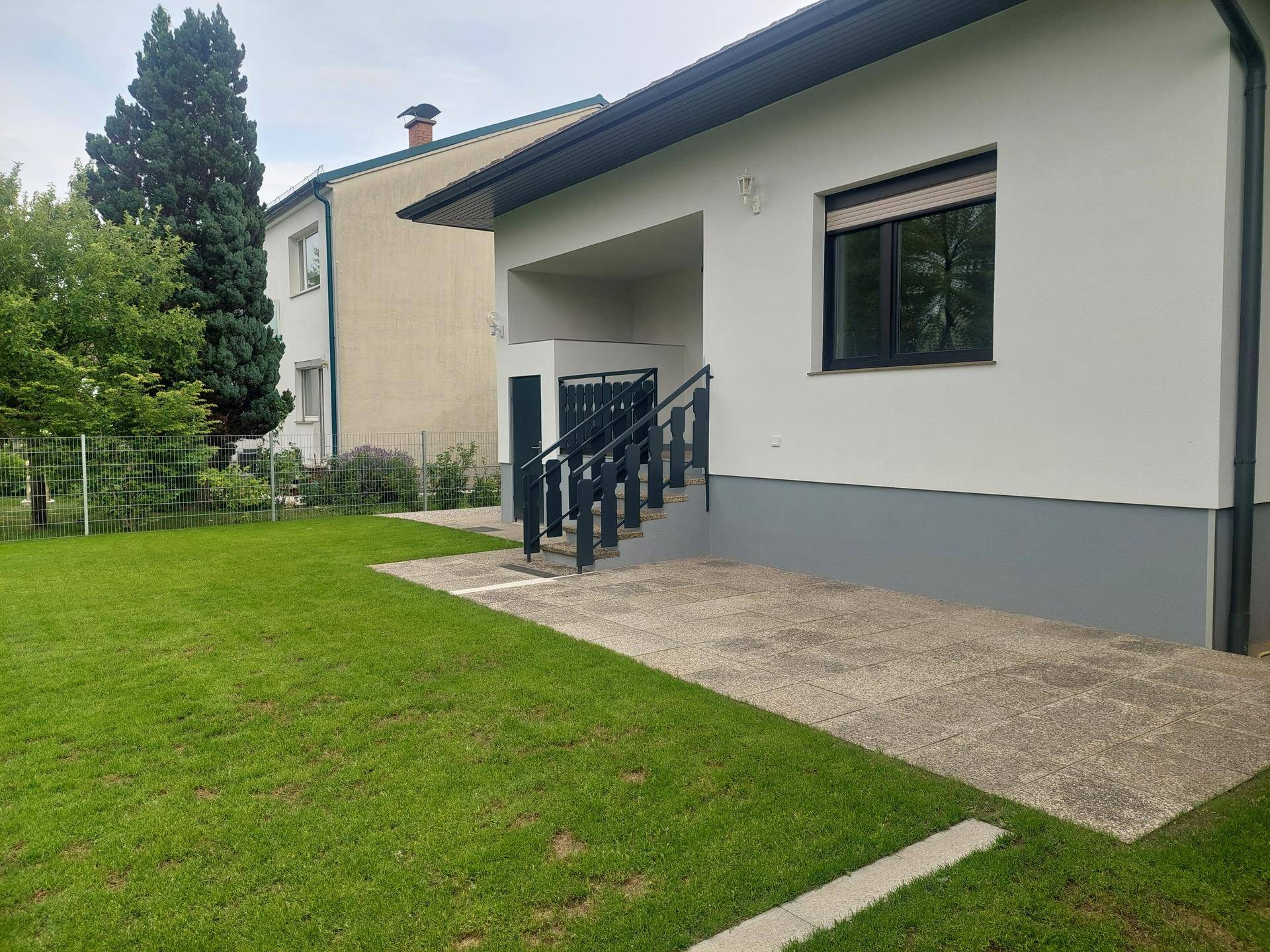 Seitenansicht des Hauses mit Rasenfläche und gepflastertem Bereich vor dem Eingang.
