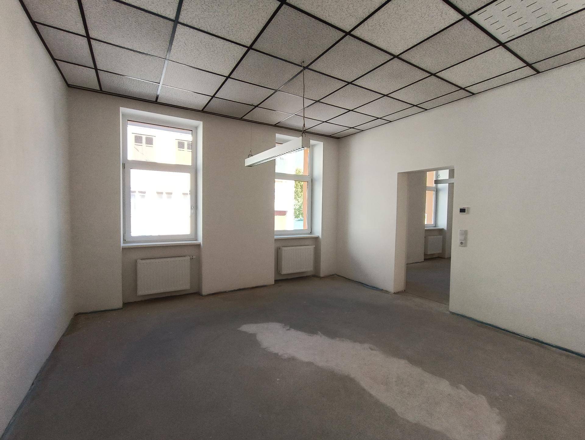 Großer, leerer Raum mit Betonboden und zwei Fenstern, ideal für individuelle Gestaltung.