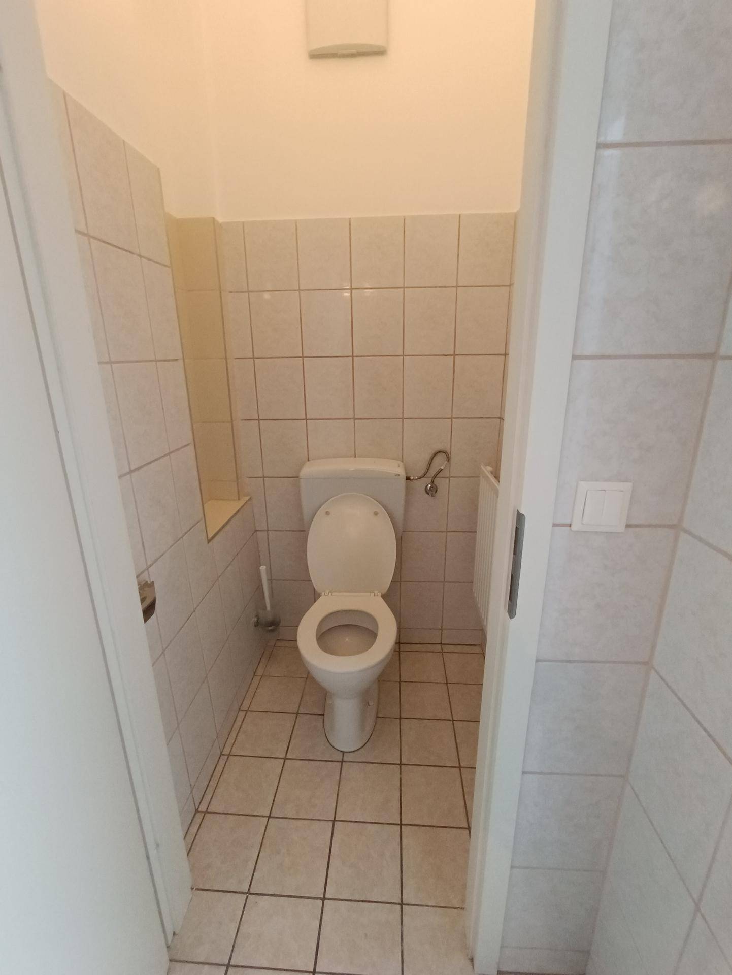 Separate Gästetoilette mit weißen Fliesen und Standard-WC, sauber und gepflegt.