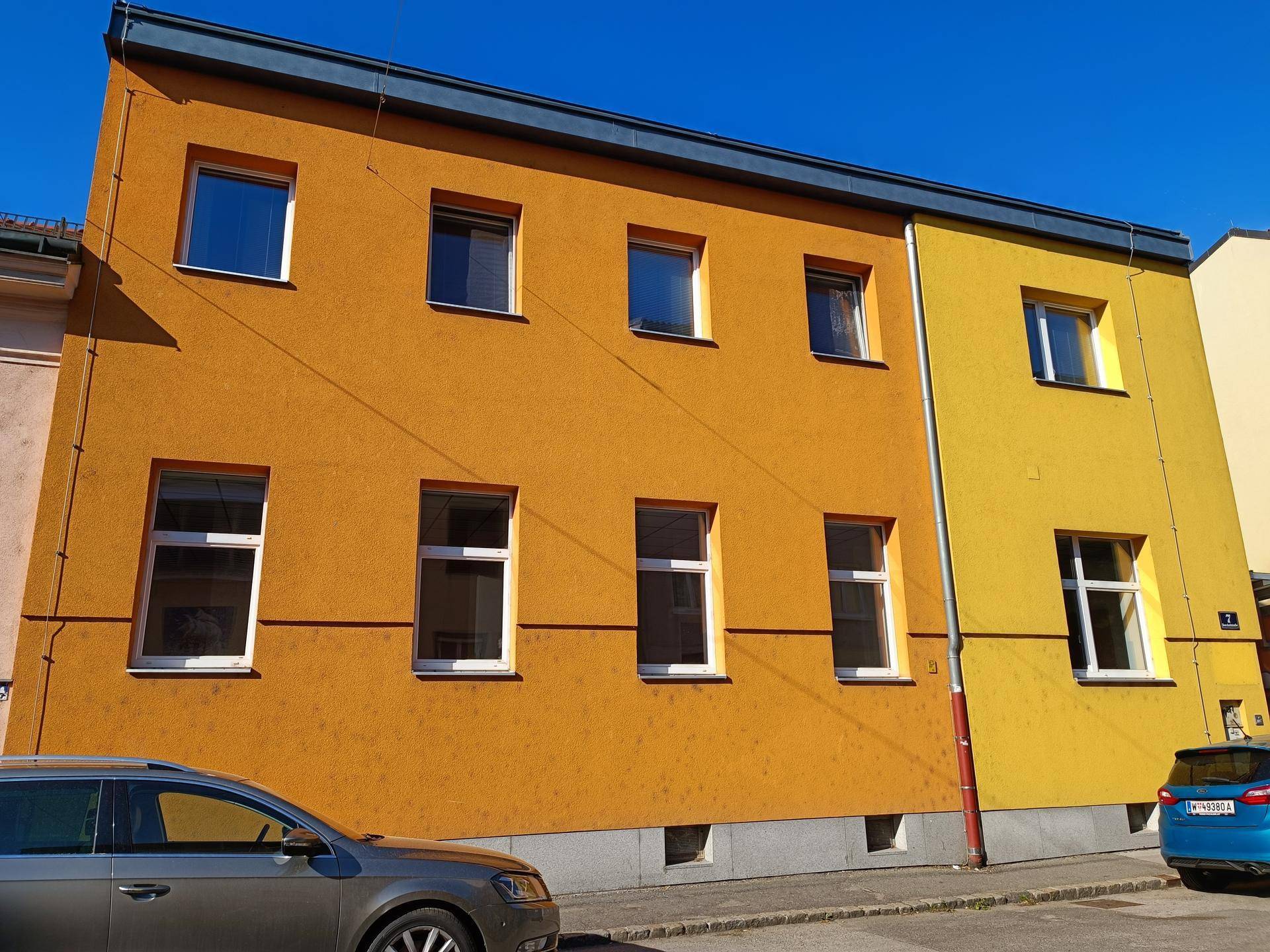 Mehrstöckiges Gebäude mit auffälliger orange-gelber Fassade und mehreren Fenstern an der Straße.