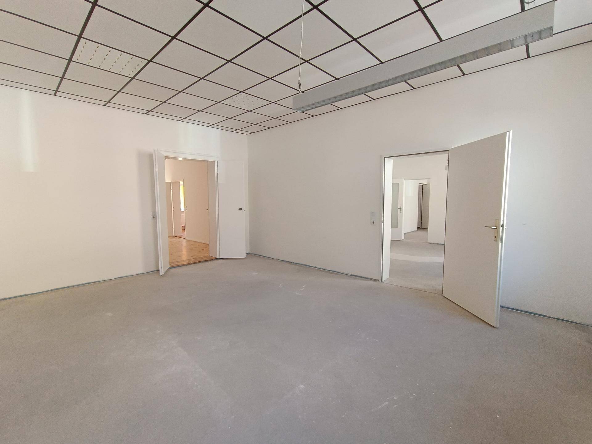 Großer, heller Raum mit Betonboden und zwei offenen Türen, wartet auf den Innenausbau.
