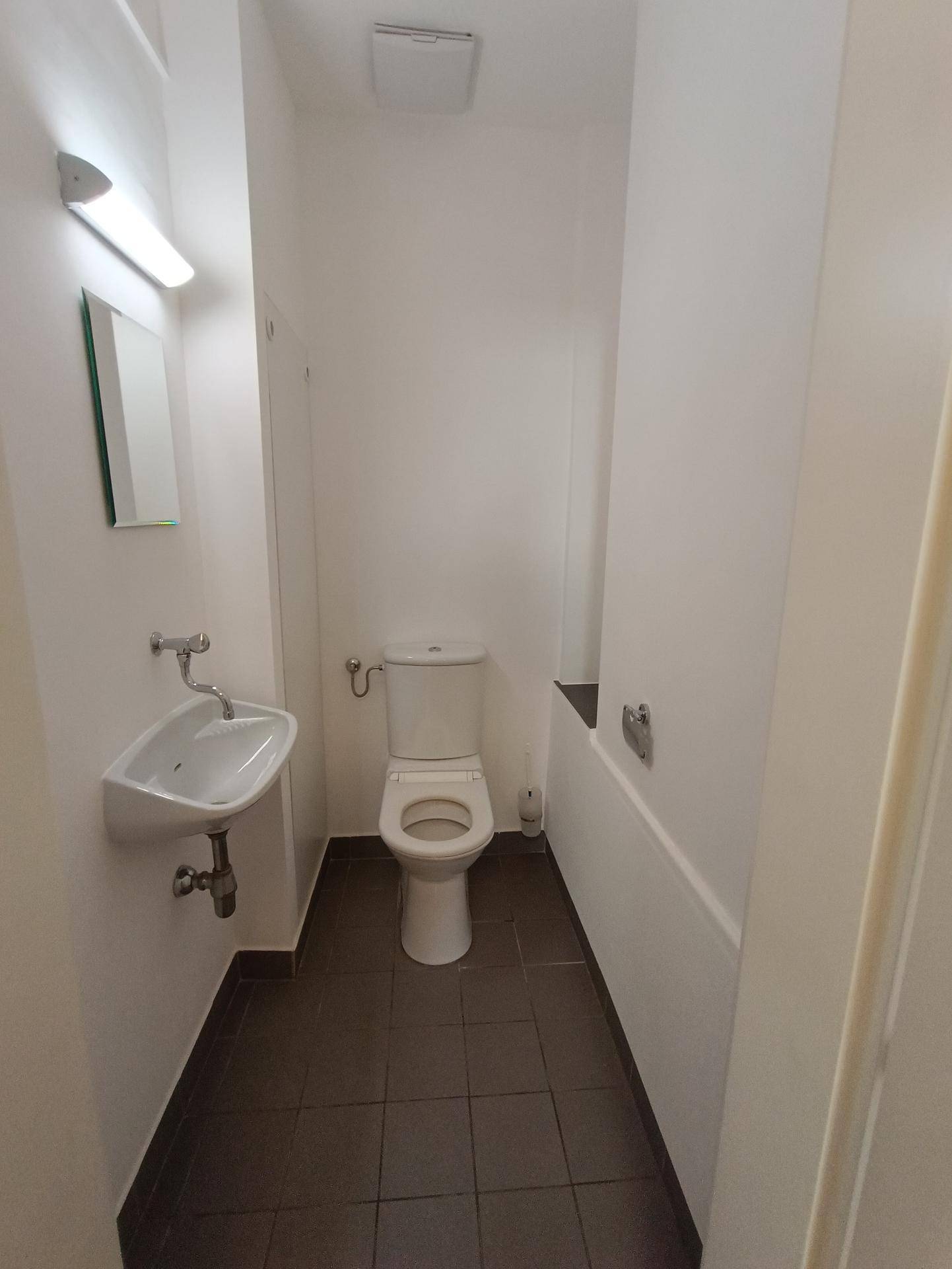 Schlichtes Badezimmer mit dunklem Fliesenboden, WC, kleinem Waschbecken und Badewanne.