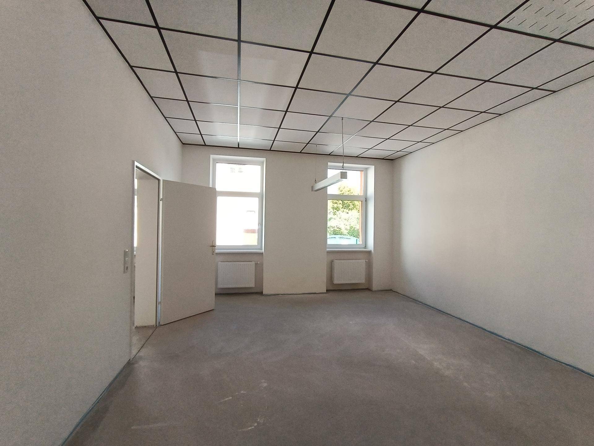 Geräumiger Raum mit Betonboden und zwei Fenstern, bietet viel Potenzial für verschiedene Nutzungen.