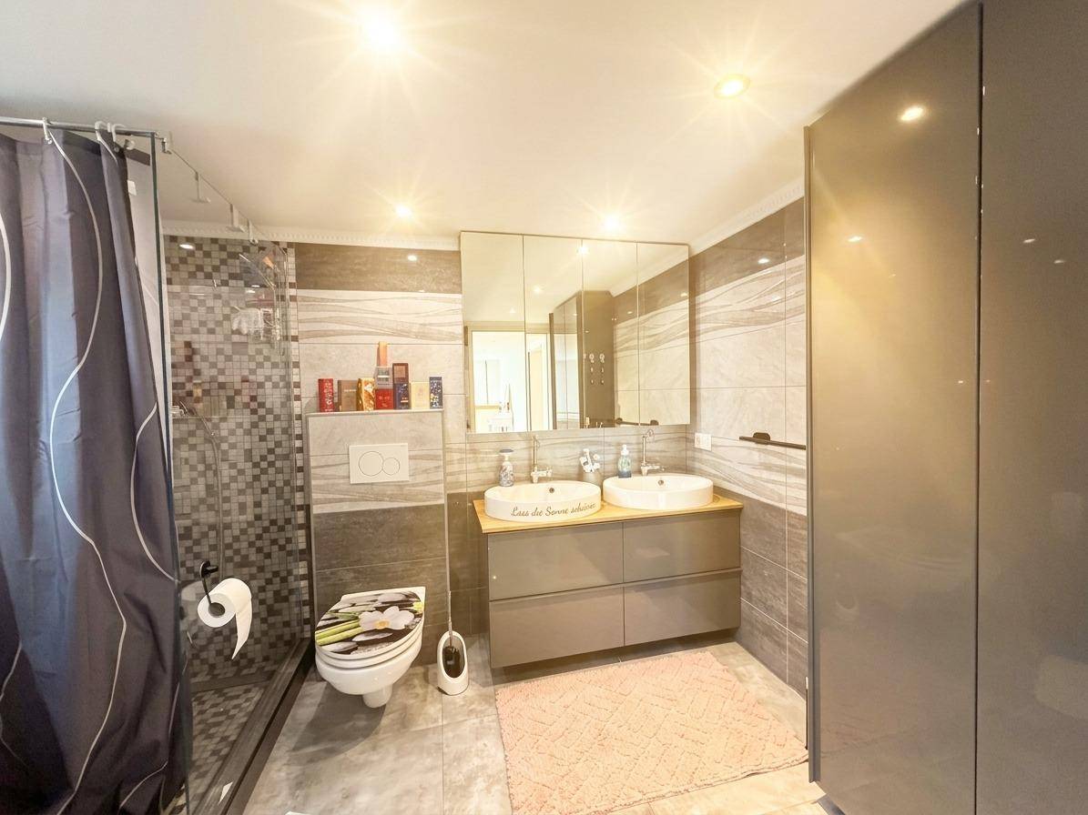 Helles Badezimmer mit Doppelwaschbecken, großer Dusche und modernen Fliesen.