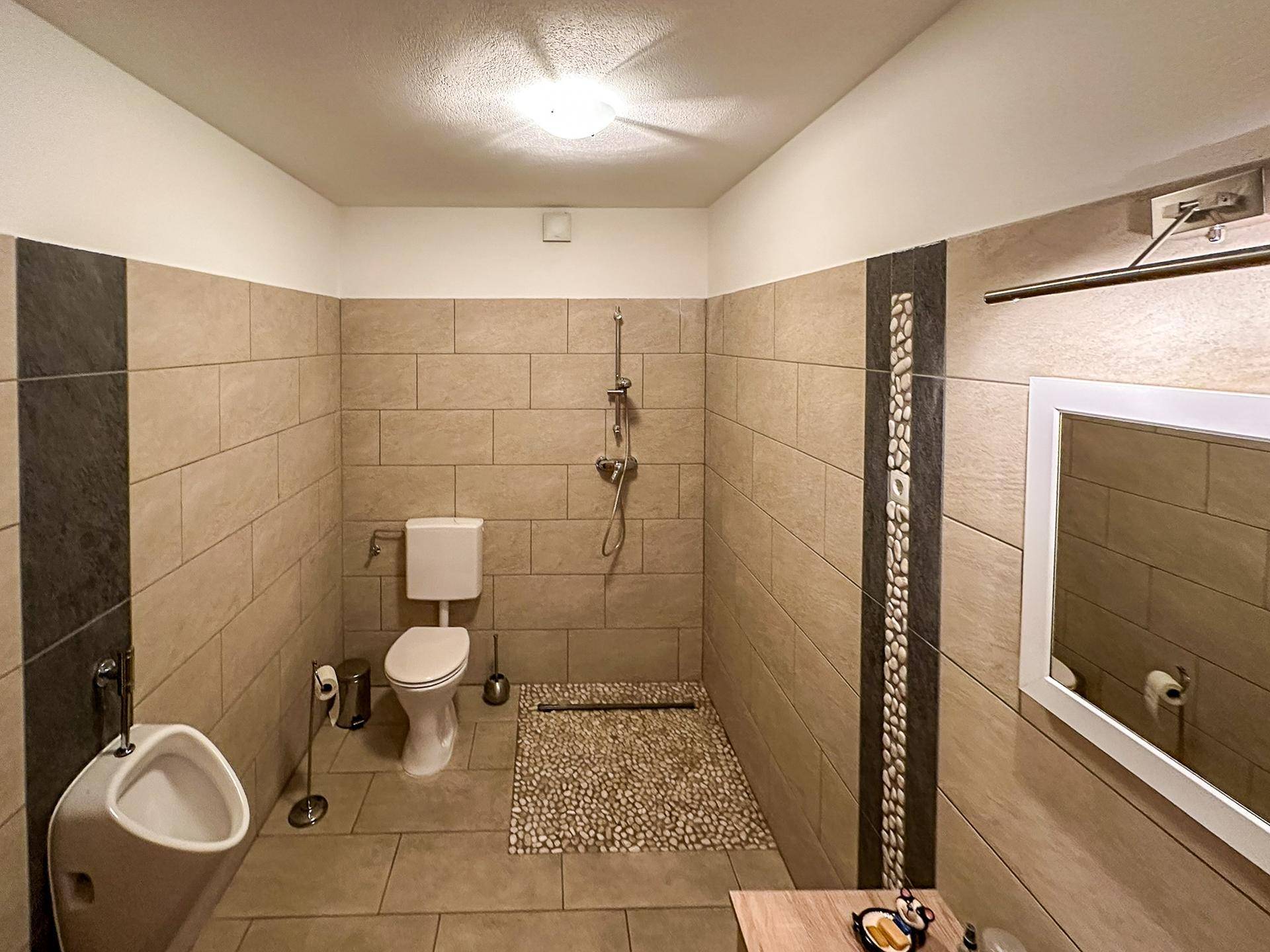 Modernes WC mit Urinal, Toilette und beigefarbenen Wandfliesen, kombiniert mit dunklen Akzenten.