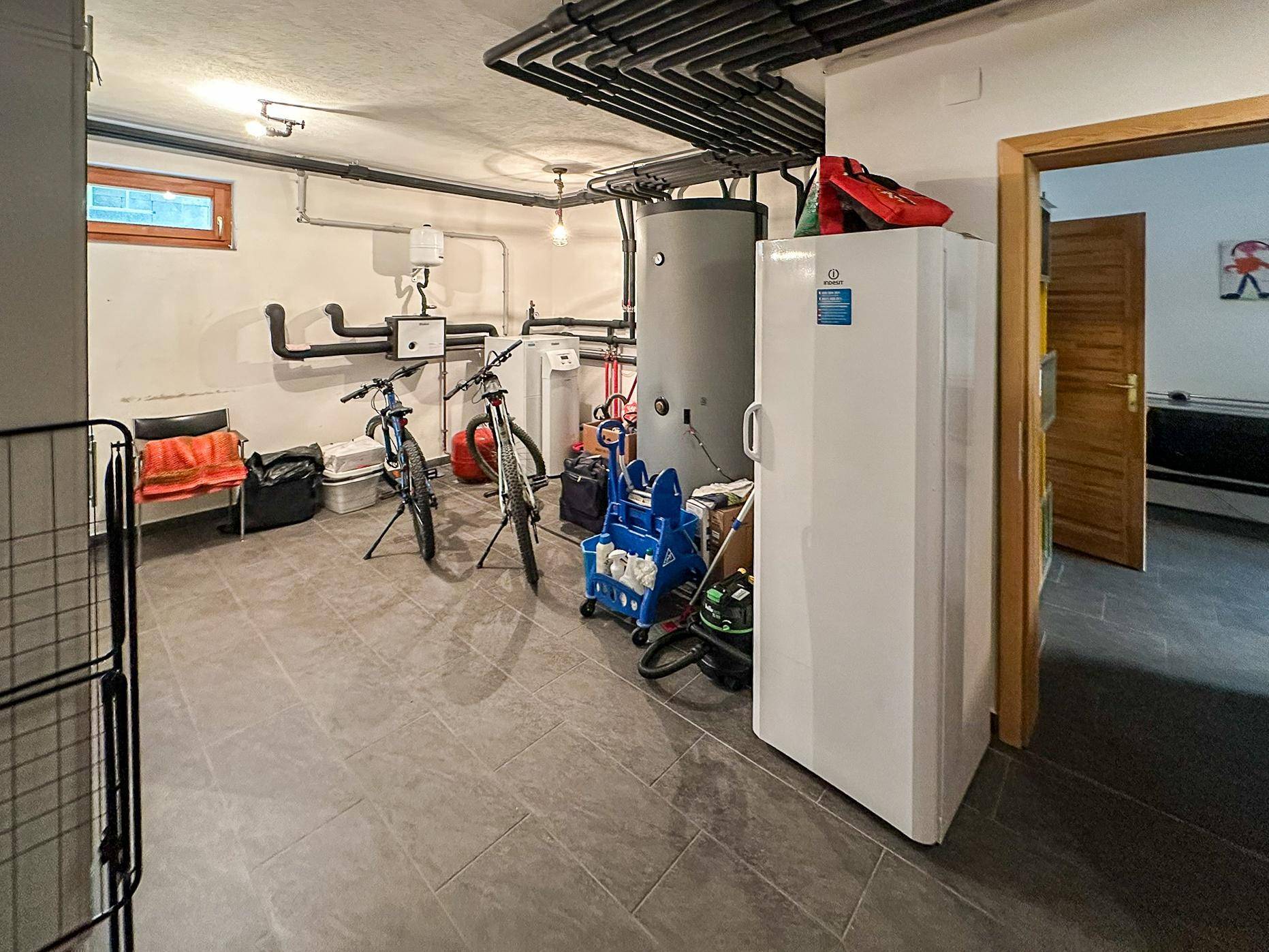 Technikraum im Keller mit Heizungsanlage, Warmwasserspeicher und sichtbaren Rohrleitungen.