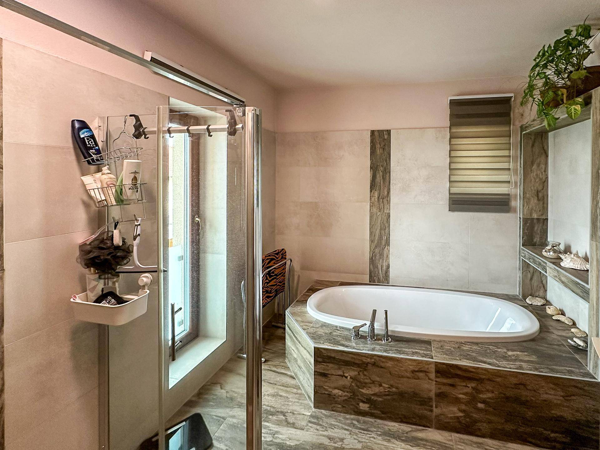 Helles Badezimmer mit Badewanne, Duschkabine und Fenster für Tageslicht.