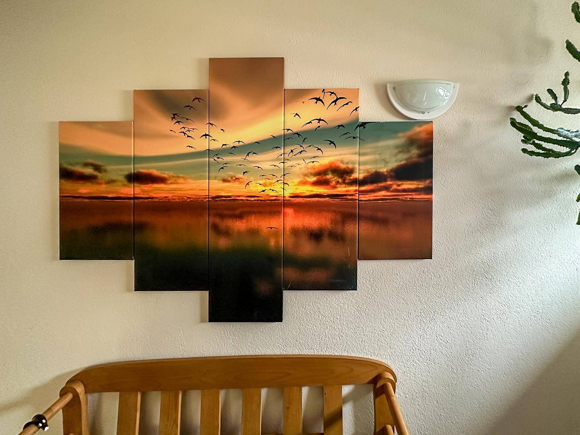 Wanddekoration mit Sonnenuntergangsmotiv und Vogelschwarm über einem Holzbett oder einer Bank.