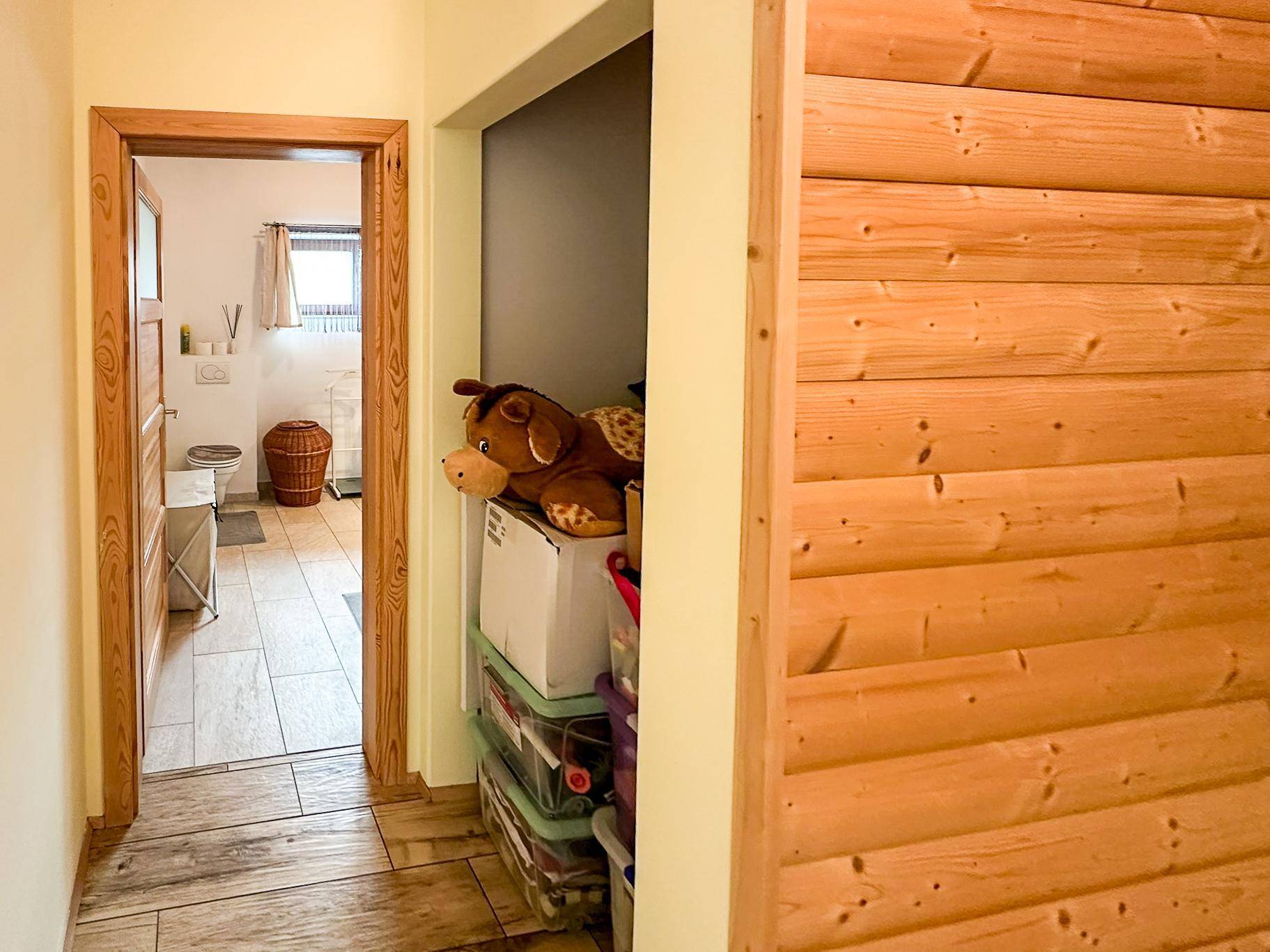 Heller Flur mit Holzwänden und Blick in ein Badezimmer, daneben ein Stauraum mit Spielzeug.