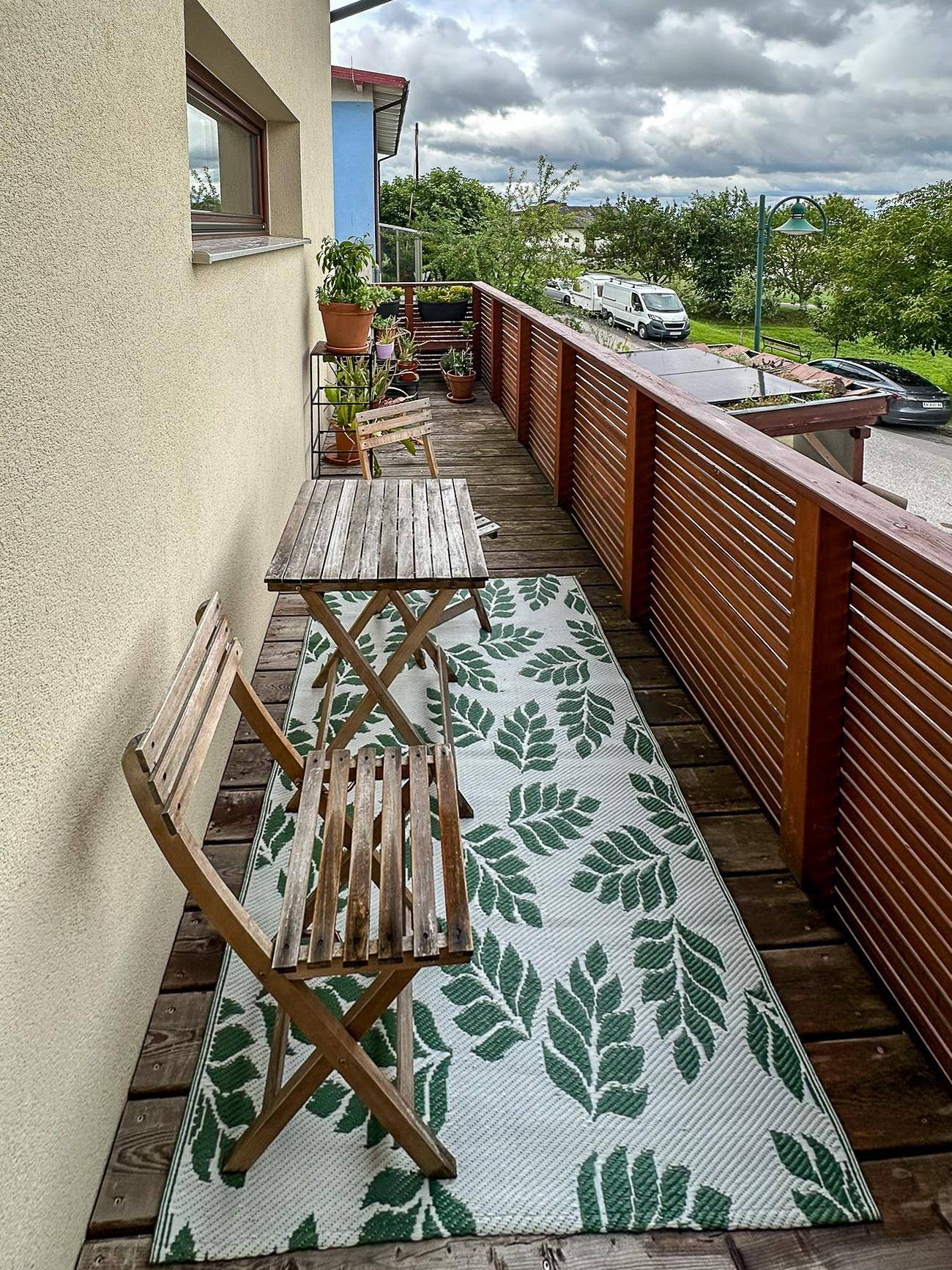 Schmaler Balkon mit Holzboden, Sitzgelegenheiten und Blick auf die Straße und umliegende Landschaft.
