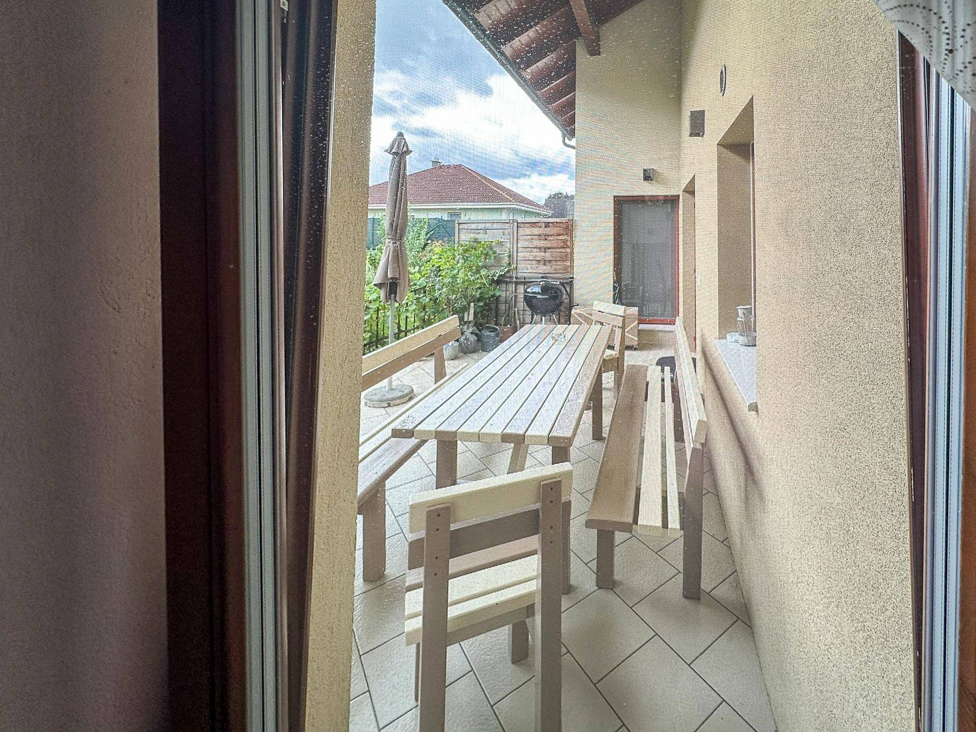 Überdachte Terrasse mit Holztisch, Bänken und Grillbereich im Freien.