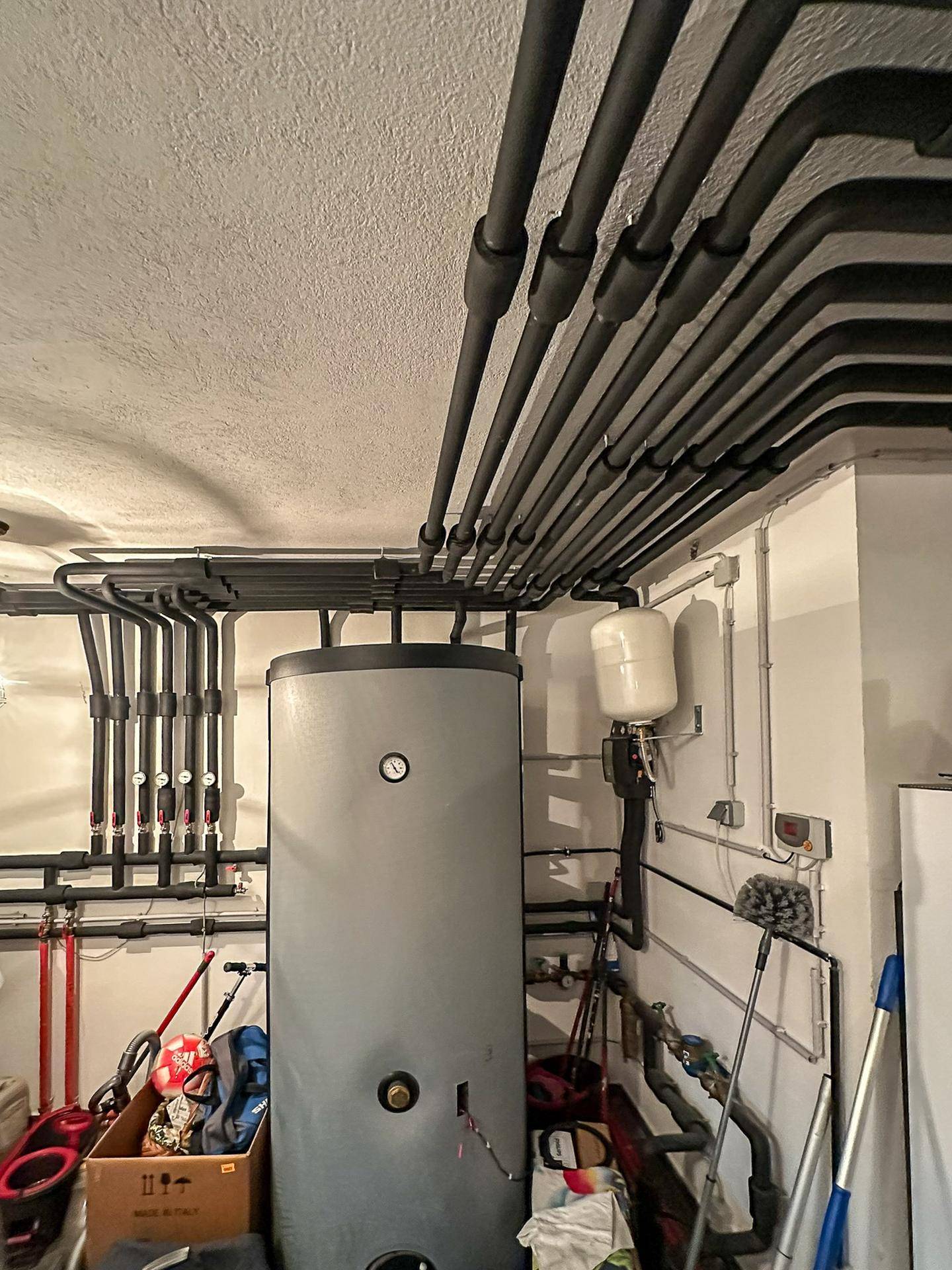 Warmwasserspeicher und umfangreiche Rohrleitungen an der Decke im Technikraum des Kellers.