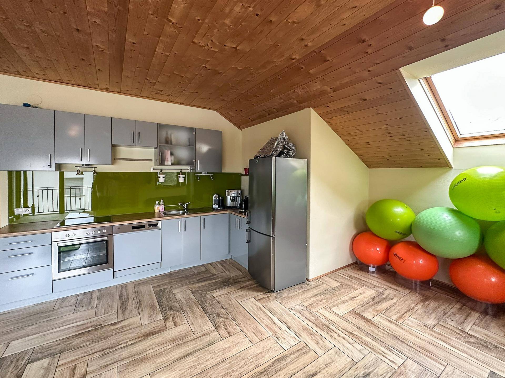 Dachgeschossküche mit grauen Schränken, Holzdecke und Dachfenster, ausgestattet mit modernen Geräten.