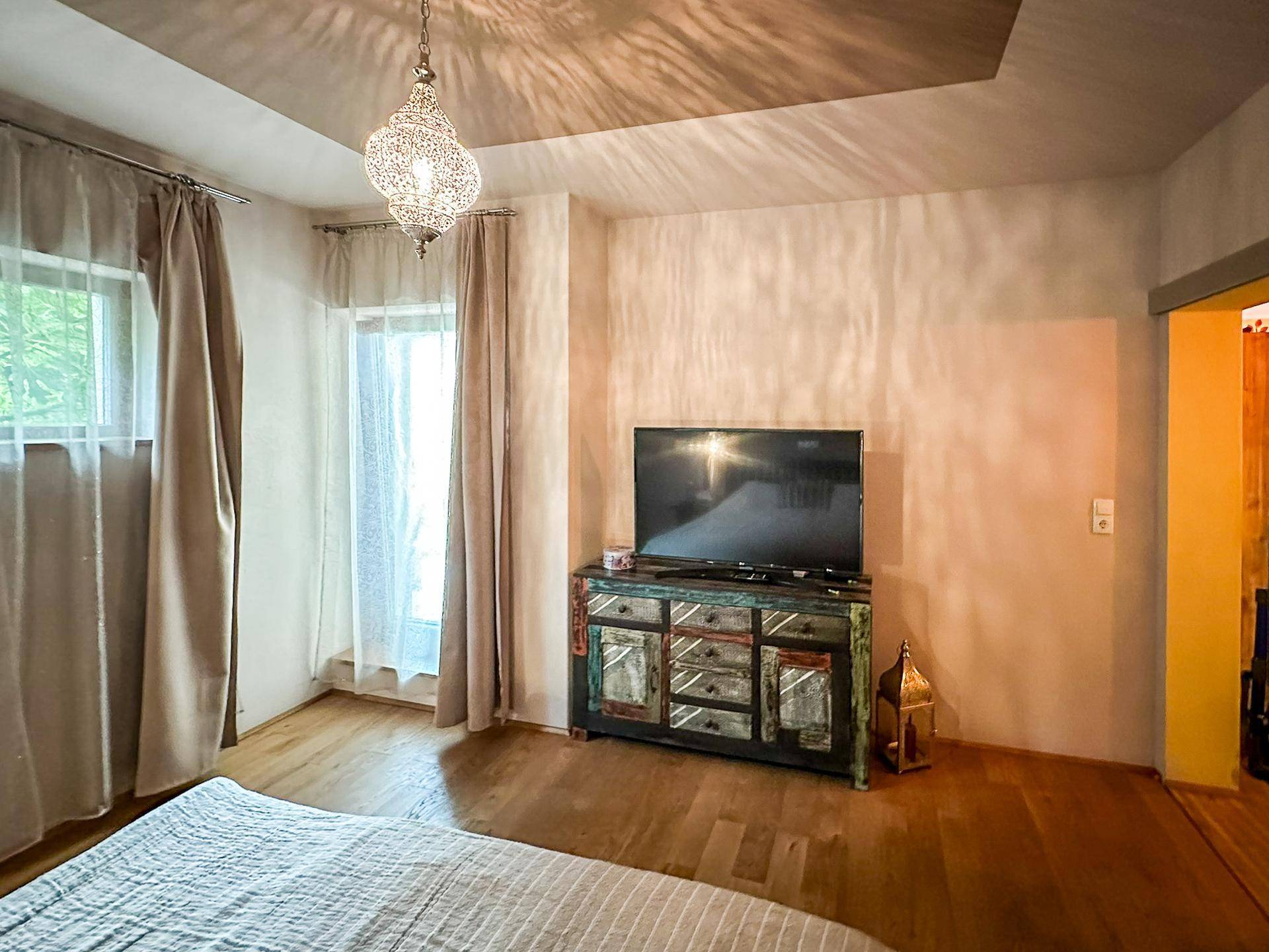 Schlafzimmer mit Holzboden, Fernseher und Zugang zu einem Balkon oder Terrasse.
