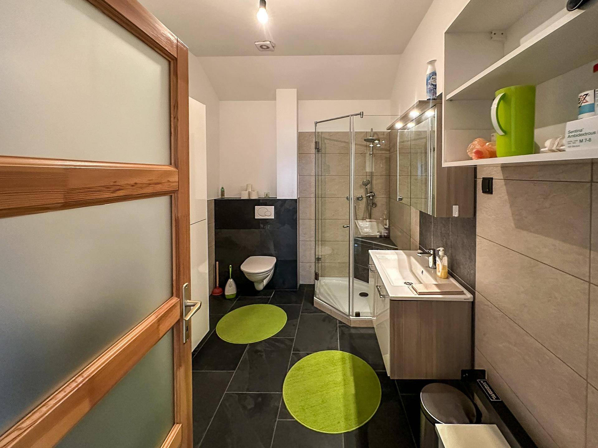 Modernes Badezimmer mit dunklen Bodenfliesen, Duschkabine und einem Waschbecken mit Unterschrank.