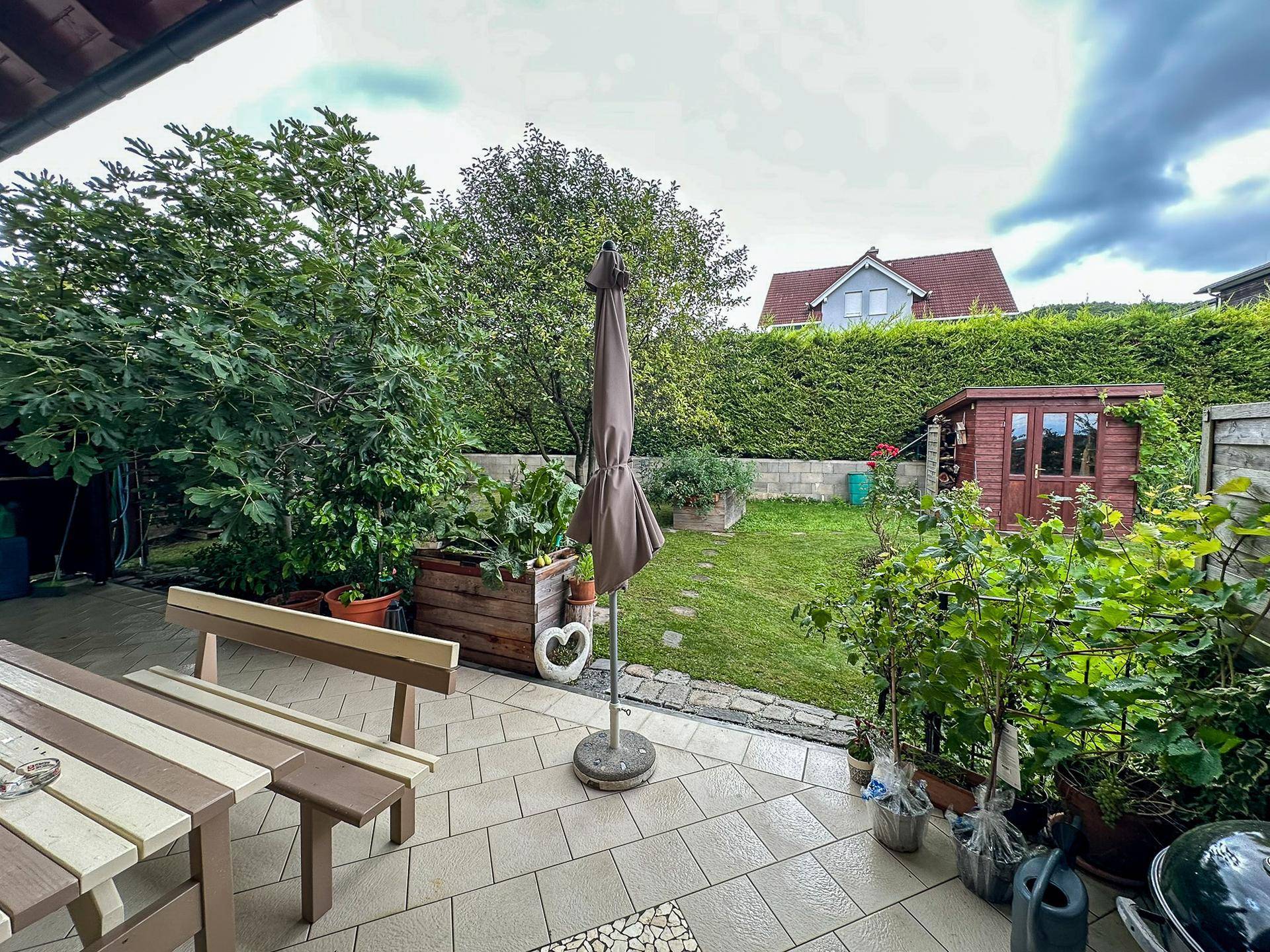 Gepflegter Garten mit Terrasse, Rasenfläche und Gartenhaus.