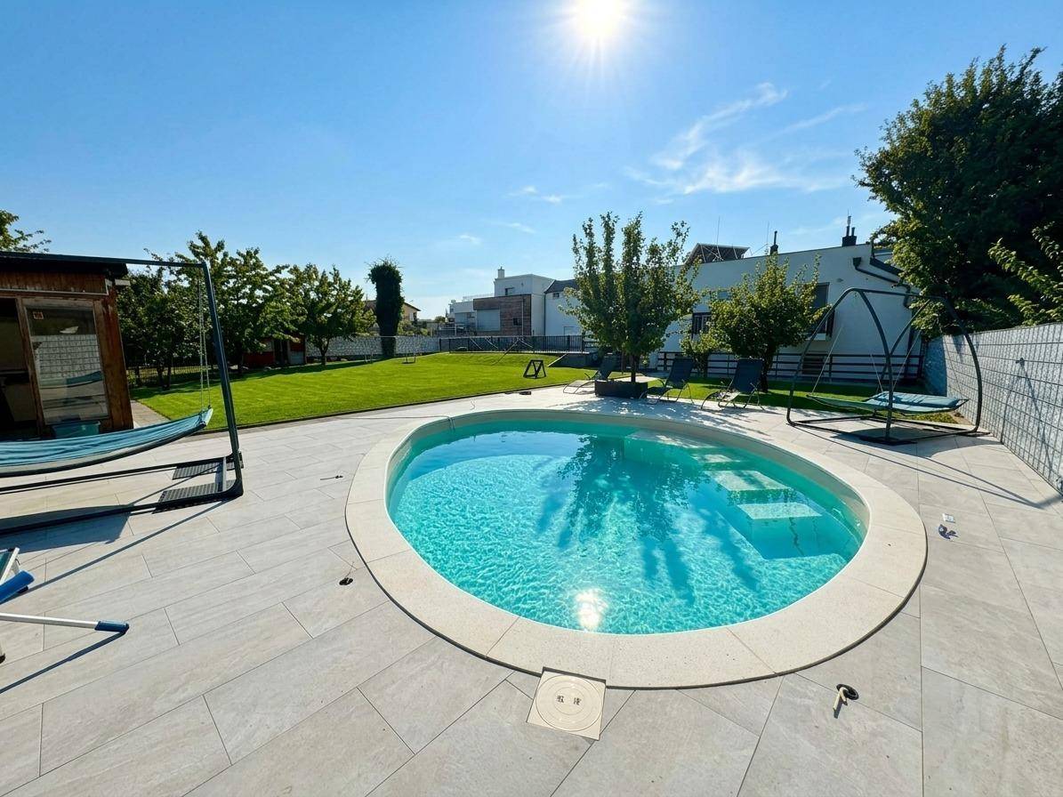 Sonniger Poolbereich mit ovalem Swimmingpool und Liegeflächen, umgeben von Grün.