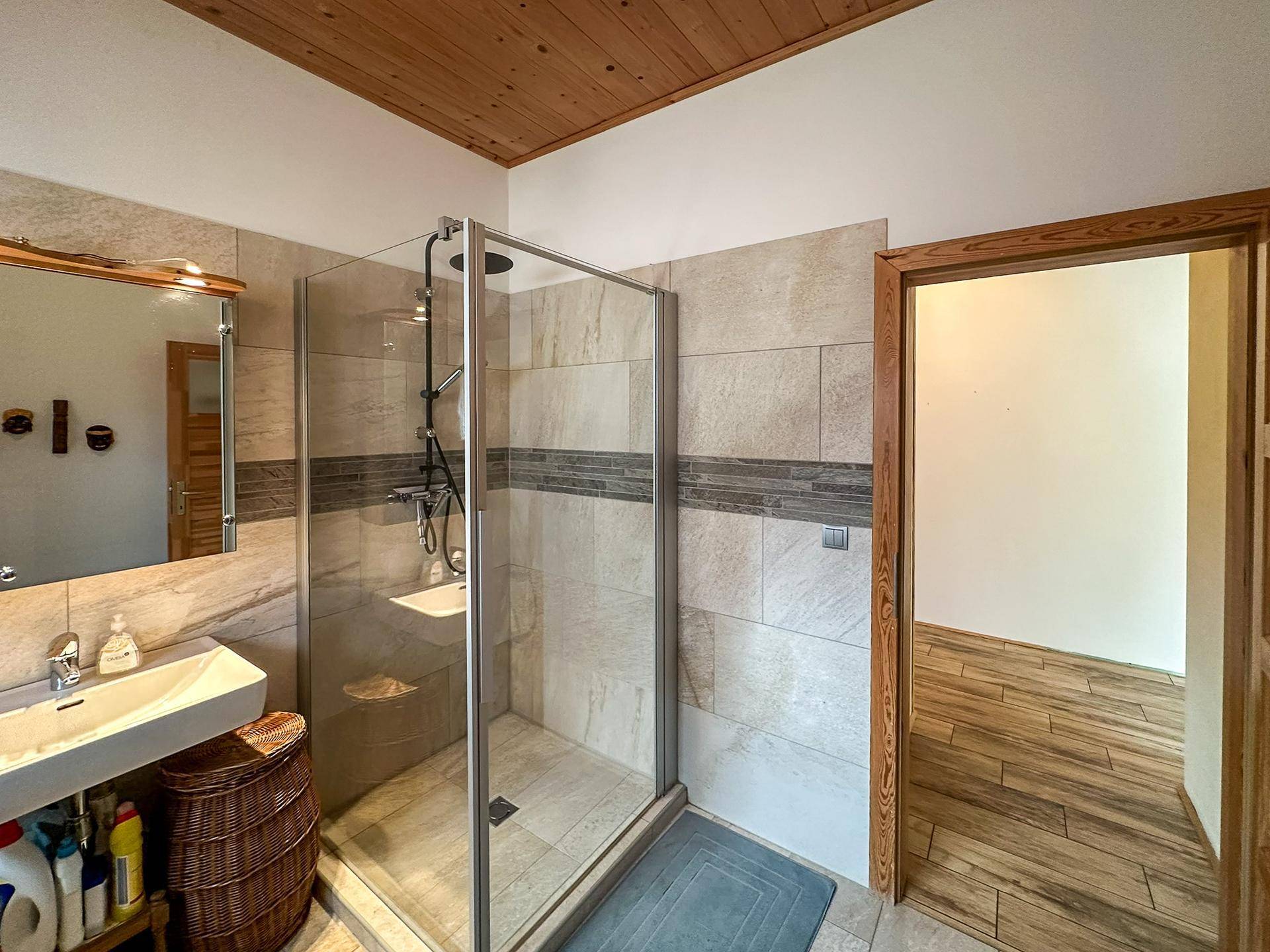 Modernes Badezimmer mit begehbarer Dusche, Holzdecke und beigefarbenen Fliesen an den Wänden.
