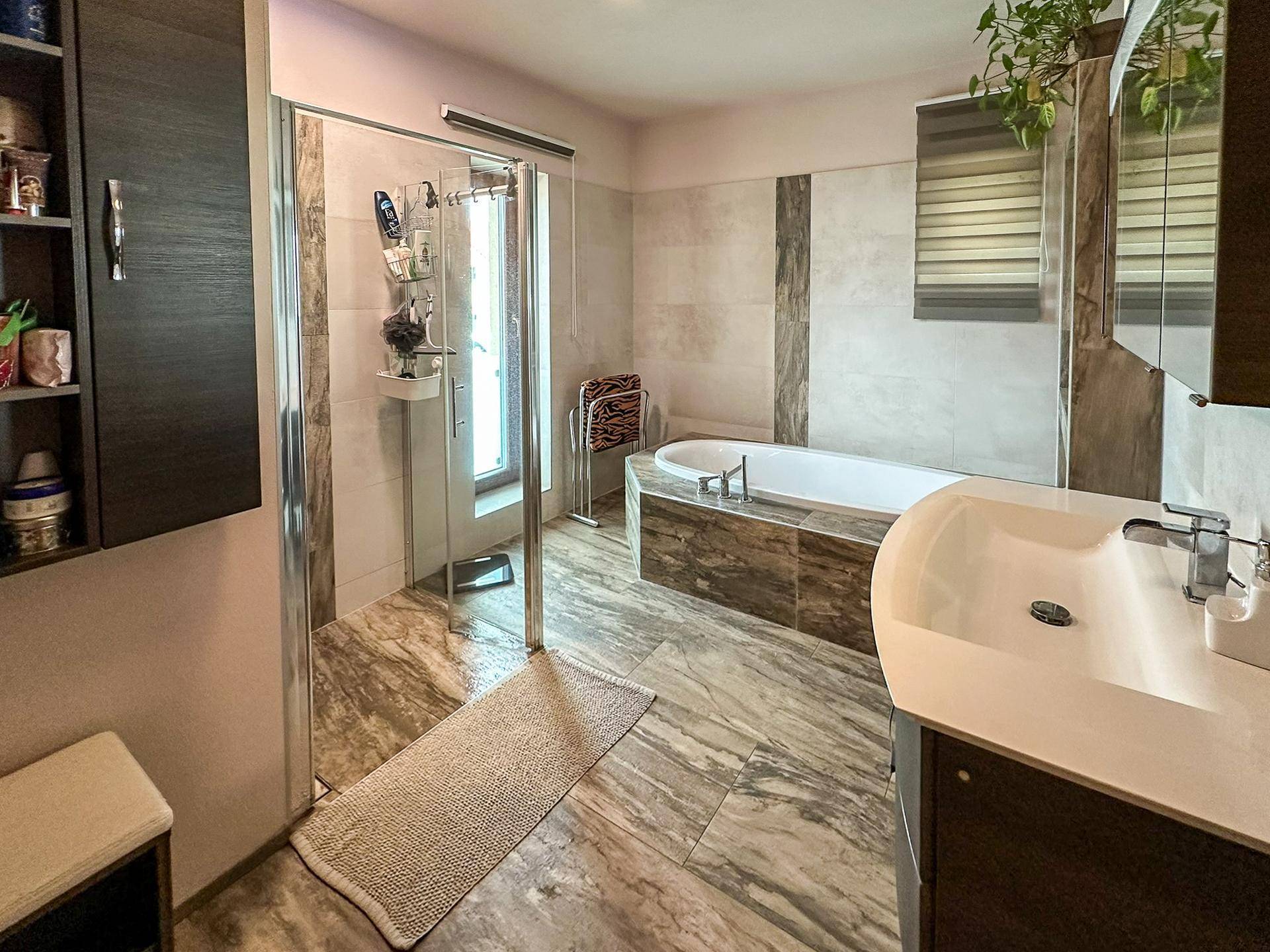 Geräumiges Badezimmer mit Badewanne, Dusche und modernen Fliesen in Erdtönen.