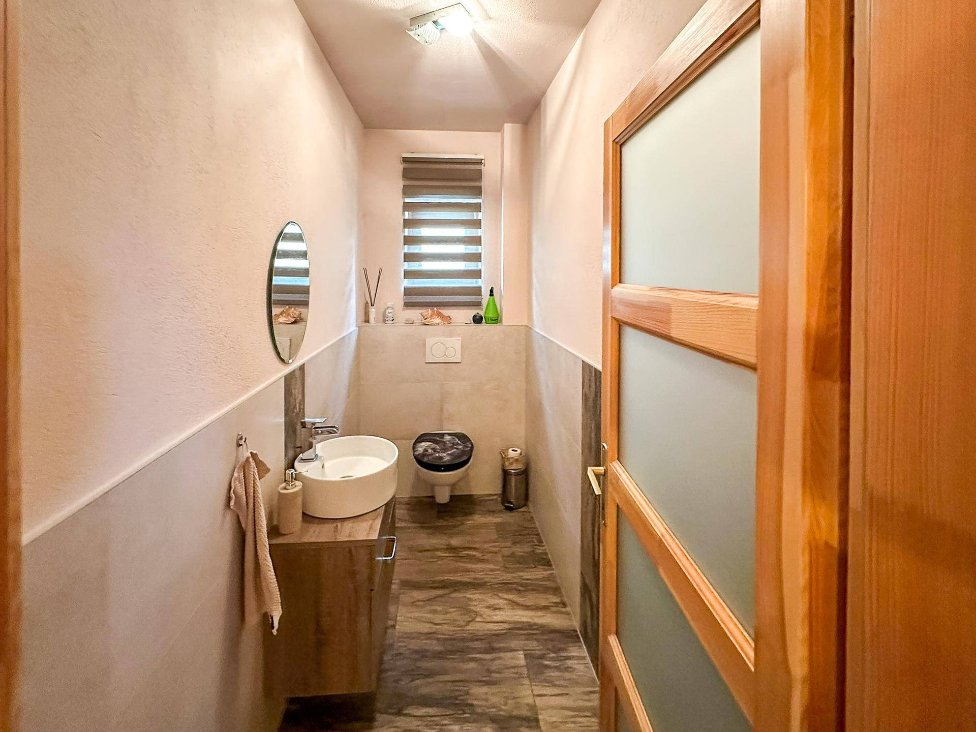 Modernes Gäste-WC mit Waschbecken, Toilette und Fenster für natürliche Belüftung.
