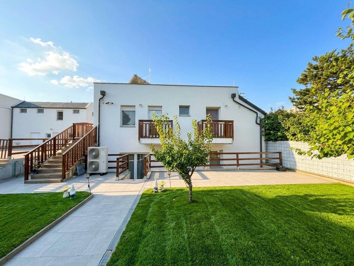 Moderne Gebäudefassade mit gepflegtem Rasen und einer großen, sonnigen Terrasse.