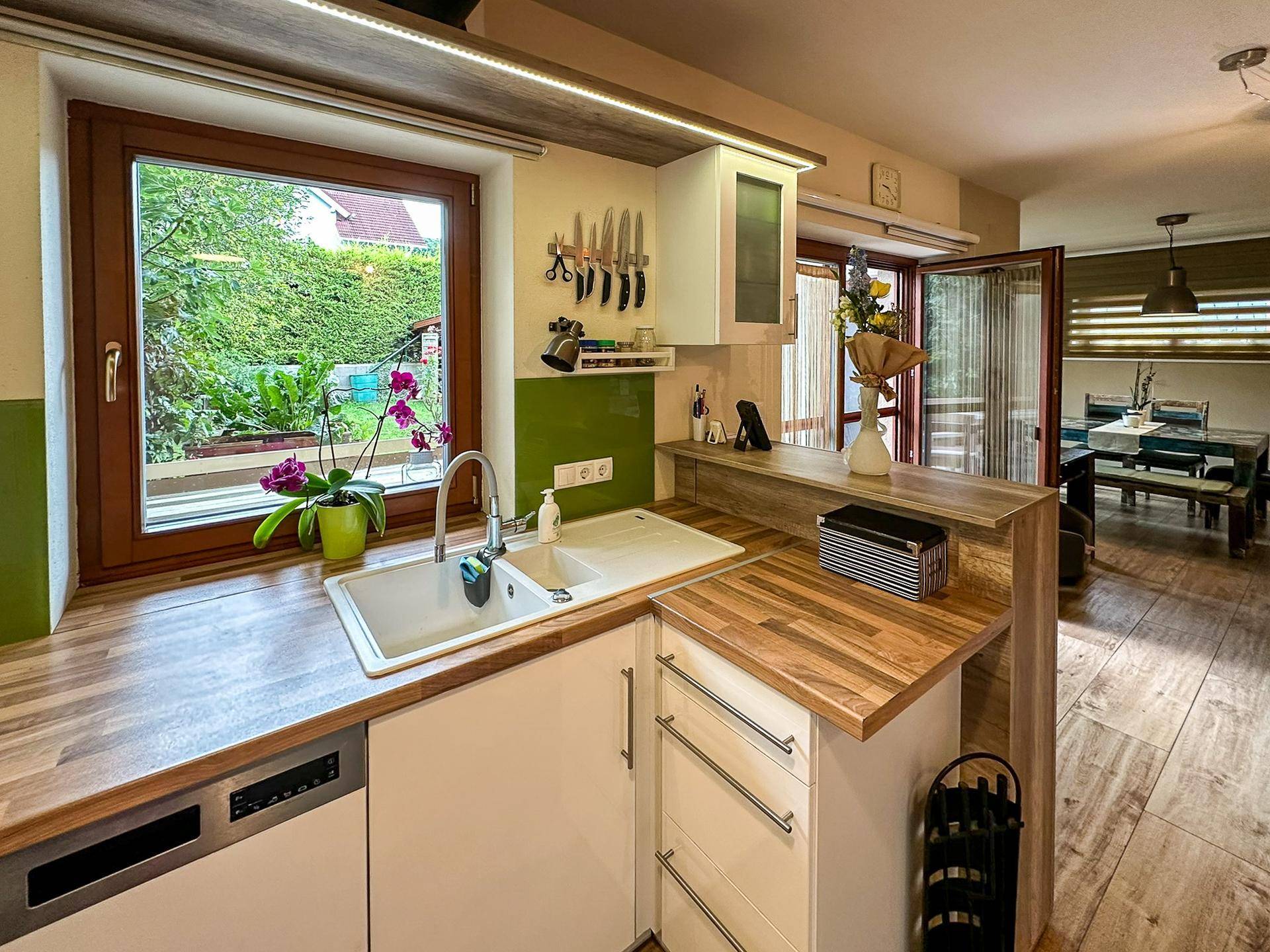 Moderne Küche mit Spülbecken, Holzarbeitsplatte und Blick in den Essbereich.