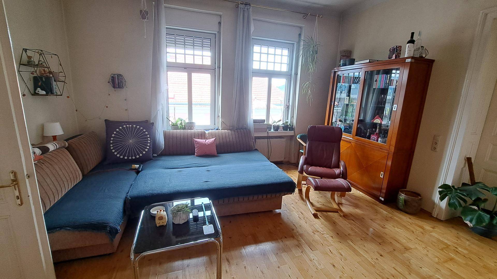 Wohnzimmer mit großem Ecksofa, Holzboden und einem klassischen Holzschrank, der Stauraum bietet.