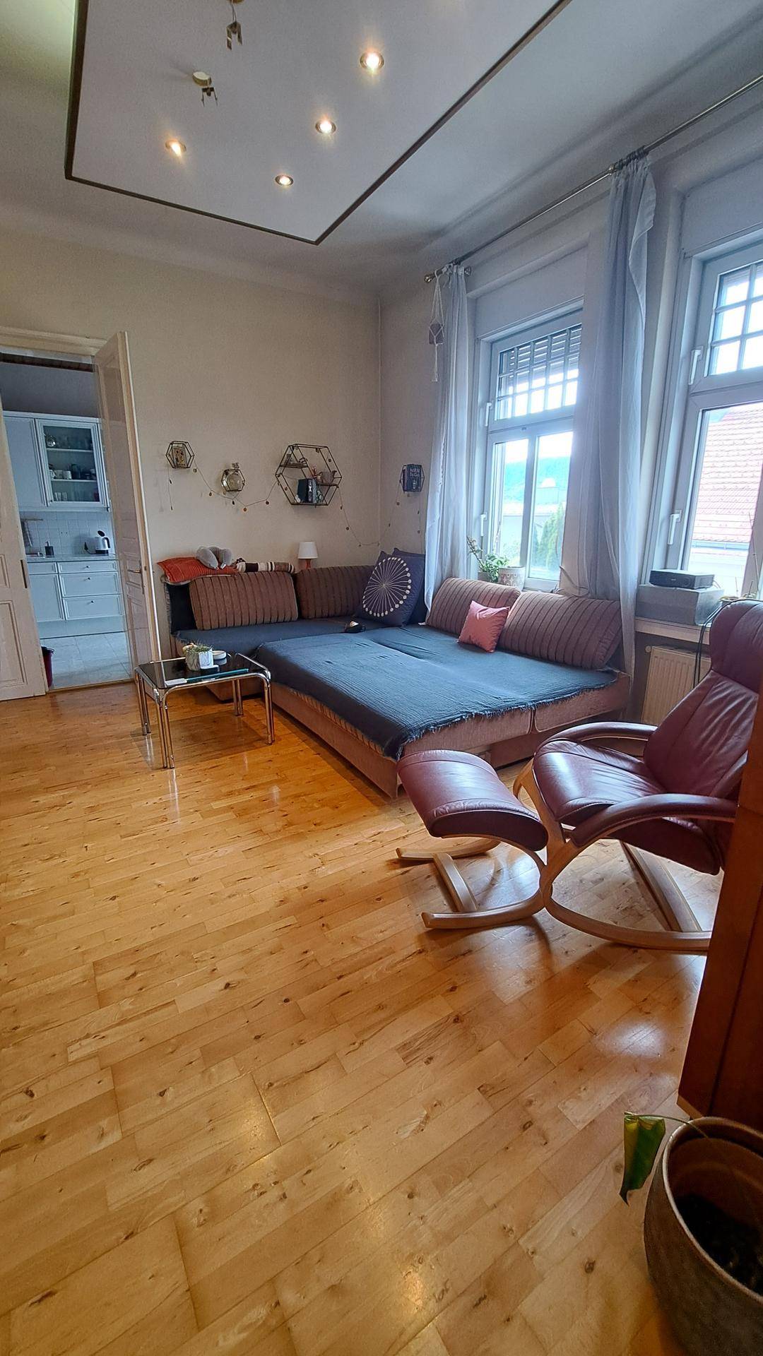 Gemütliches Wohnzimmer mit Holzboden, großem Sofa und einem bequemen Ledersessel, ideal zum Entspannen.