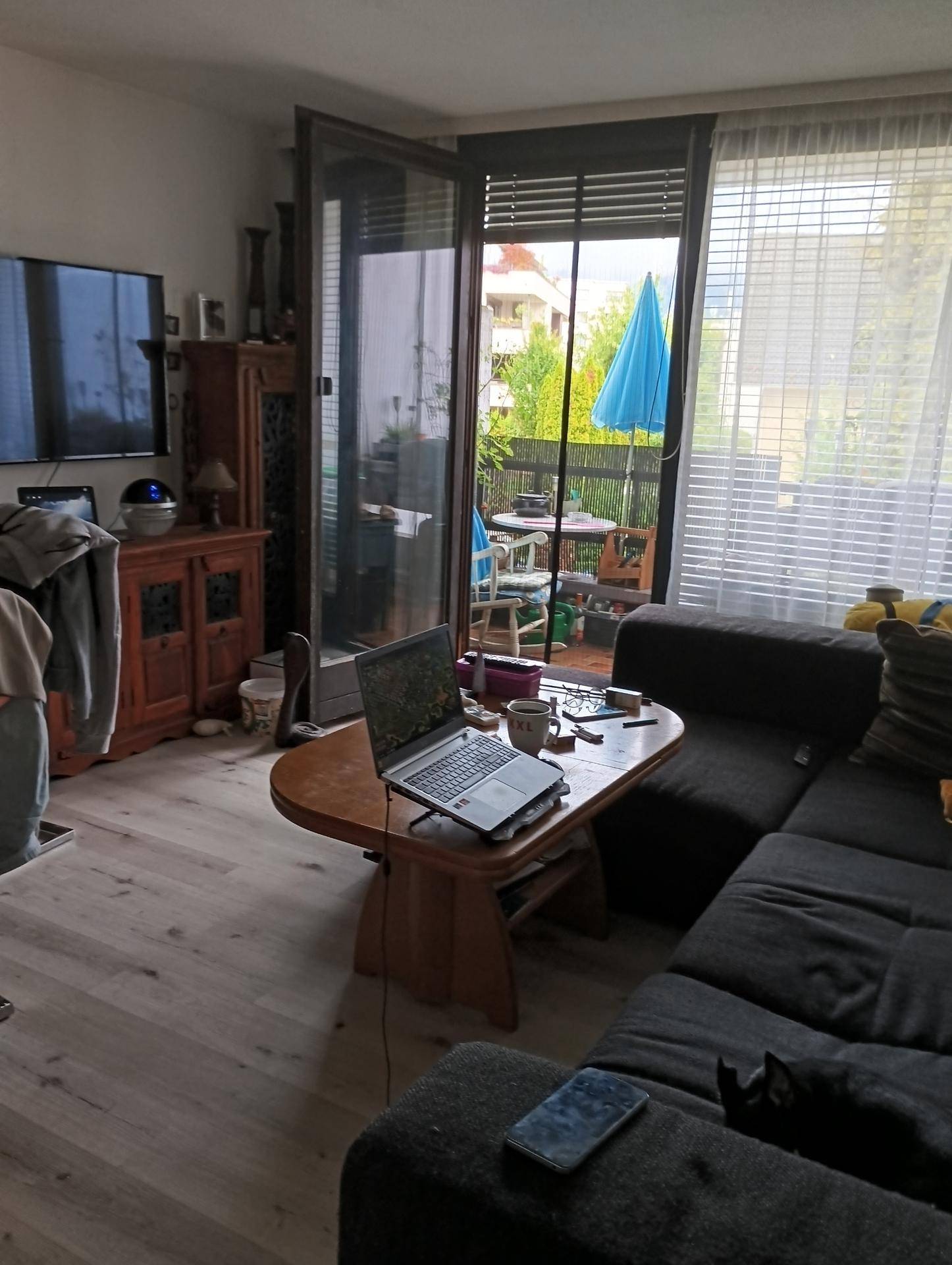 Helles Wohnzimmer mit Sofa, Couchtisch und direktem Zugang zu einem Balkon mit Sonnenschirm.