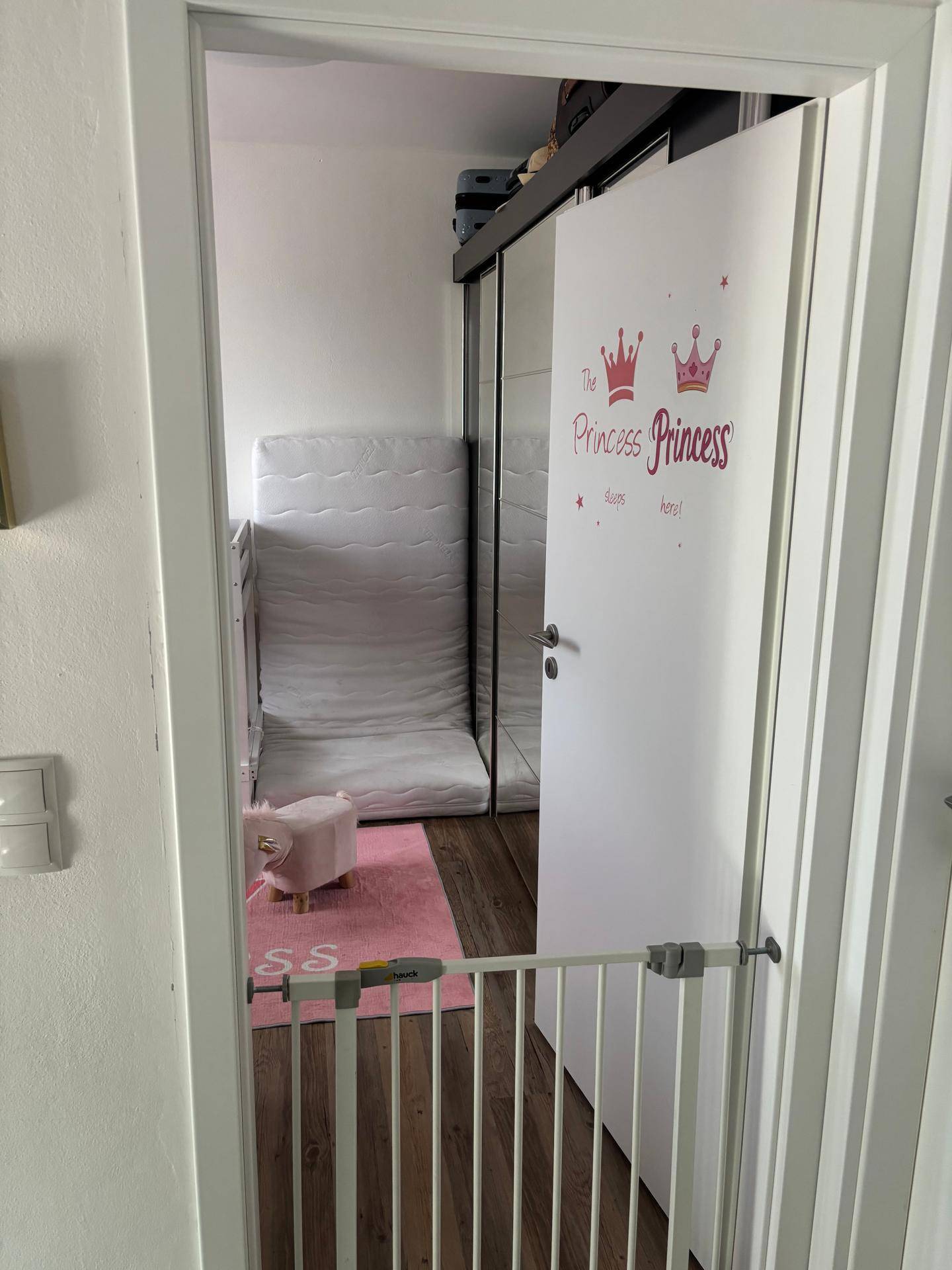 Kinderzimmer mit rosa Teppich, Schiebetürenschrank und einem Kinderbett.