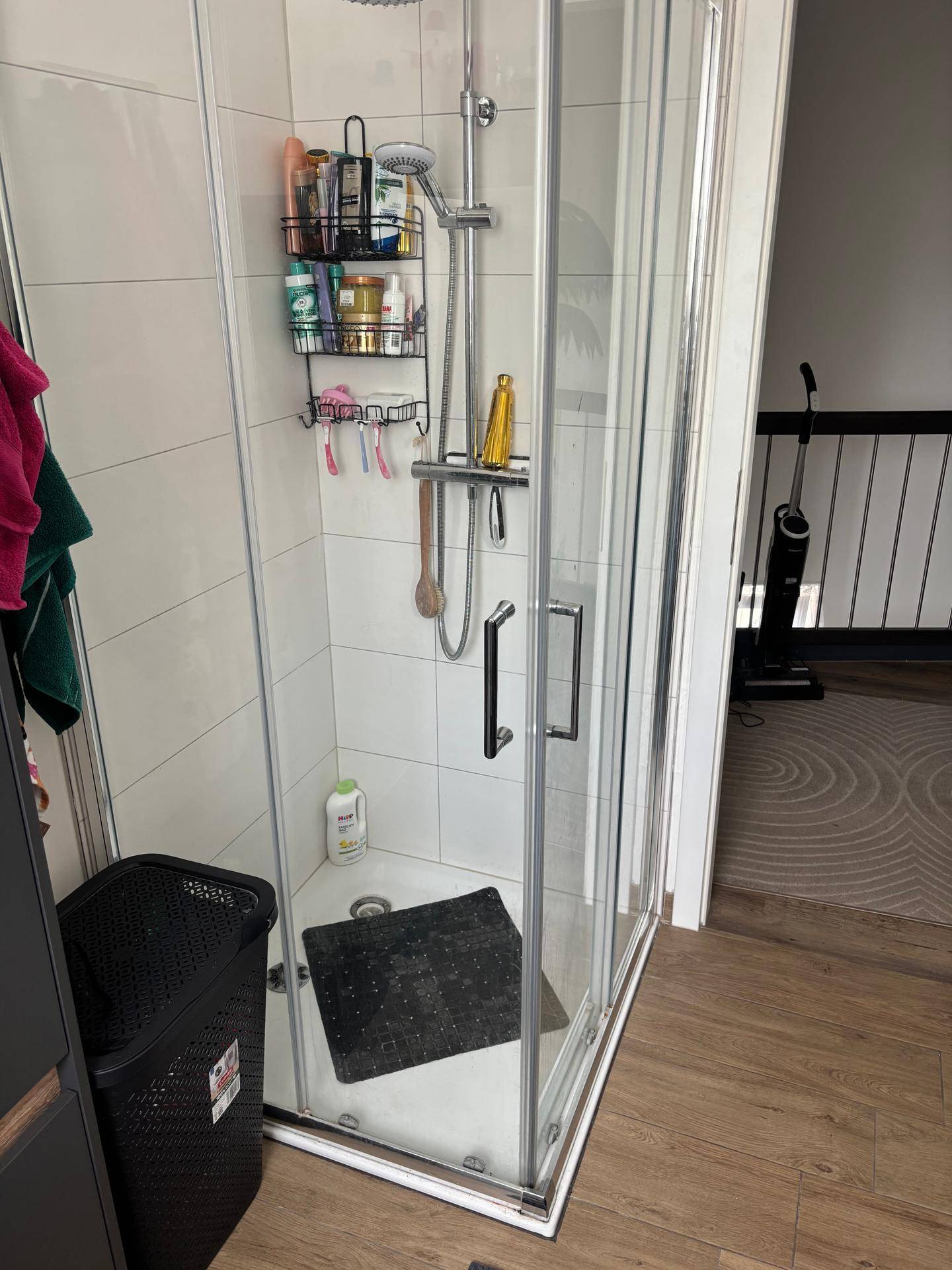 Moderne Duschkabine mit Glaswänden und praktischem Duschregal in hellem Badezimmer.
