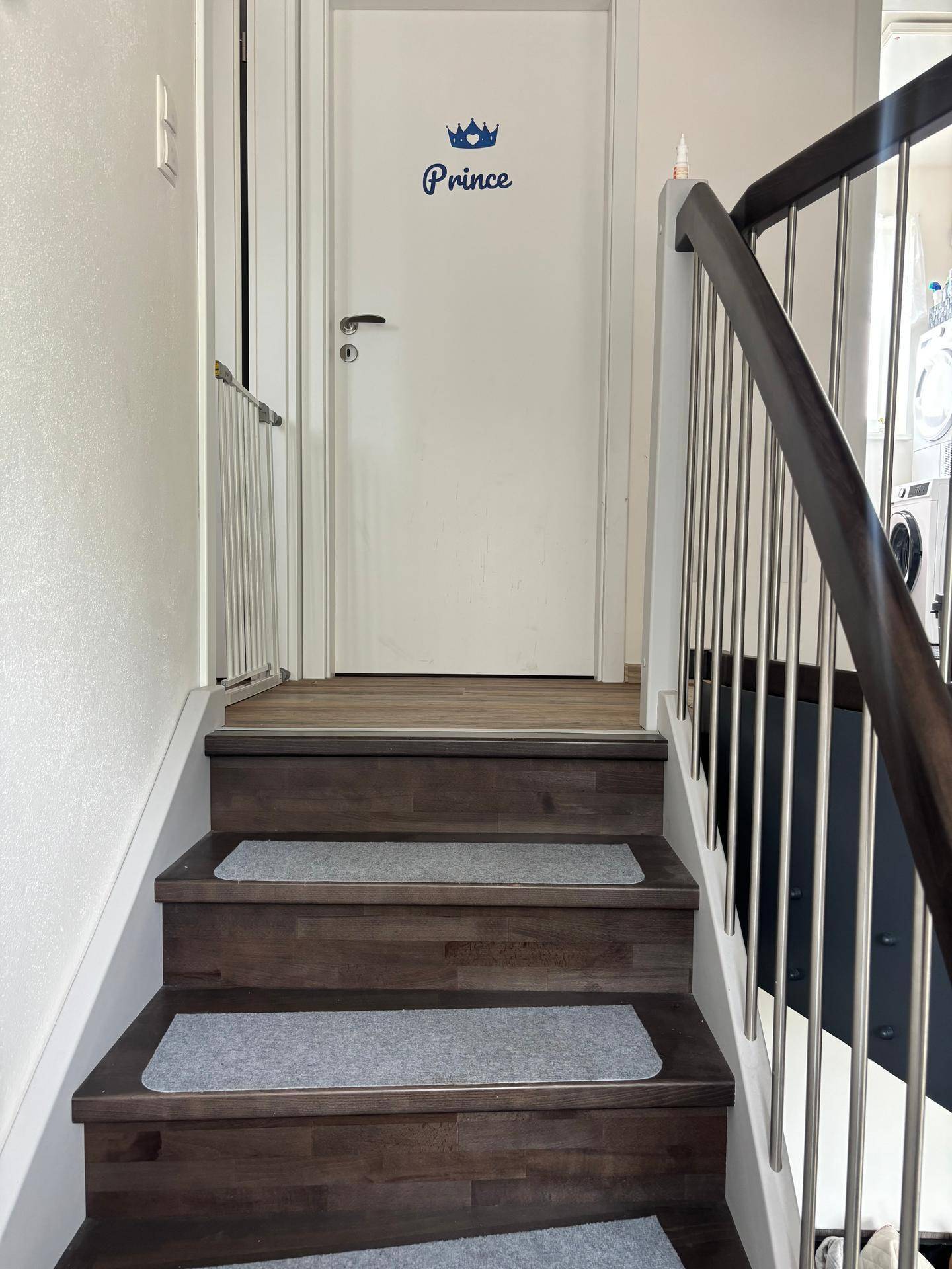 Holztreppe mit Kinderschutzgitter und einer weißen Tür mit "Prince"-Aufschrift.