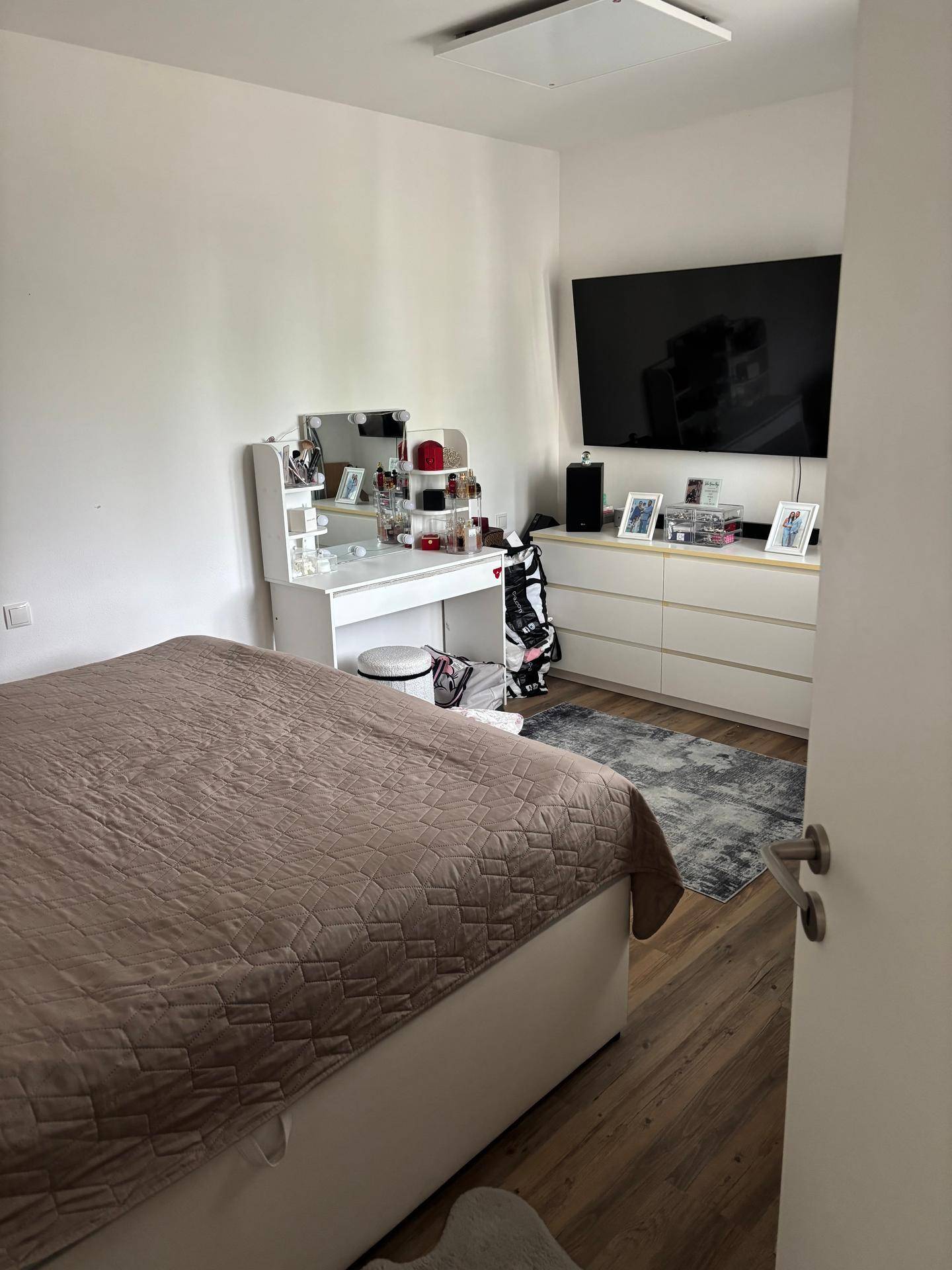 Helles Schlafzimmer mit großem Bett, Schminktisch, Wandfernseher und Laminatboden.